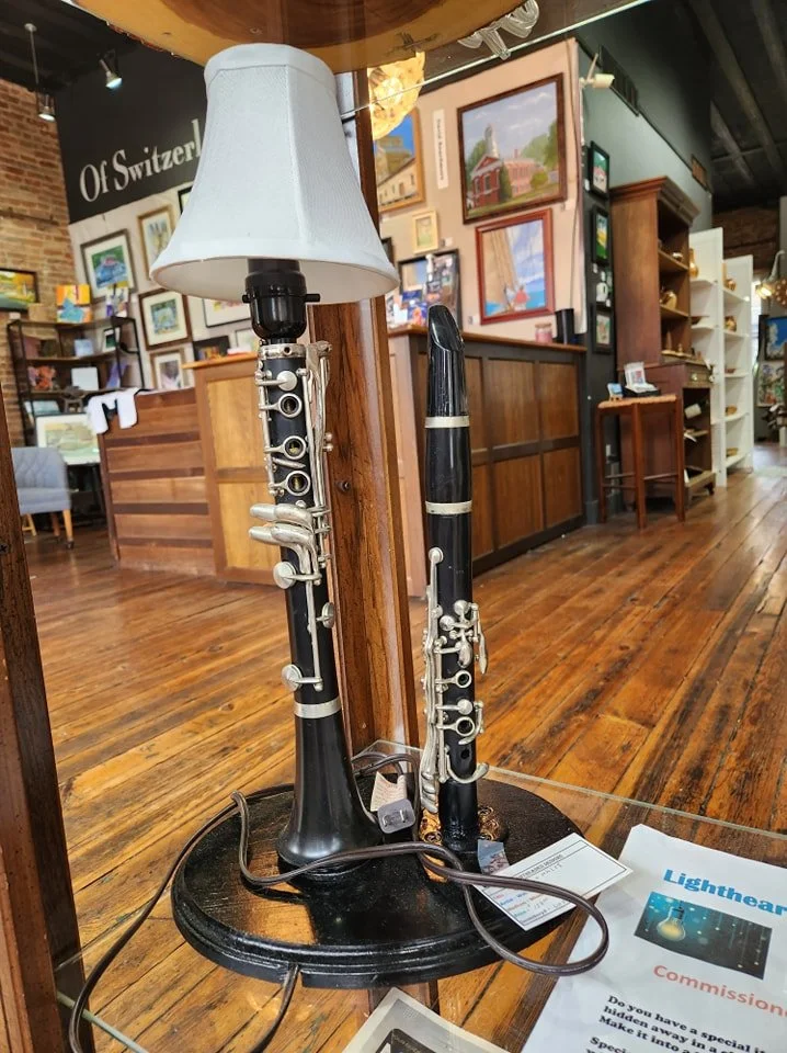 Two lamps made from musical instruments, a saxophone and a clarinet, in a bookstore or gift shop. The lamps are mounted on a small round black table.