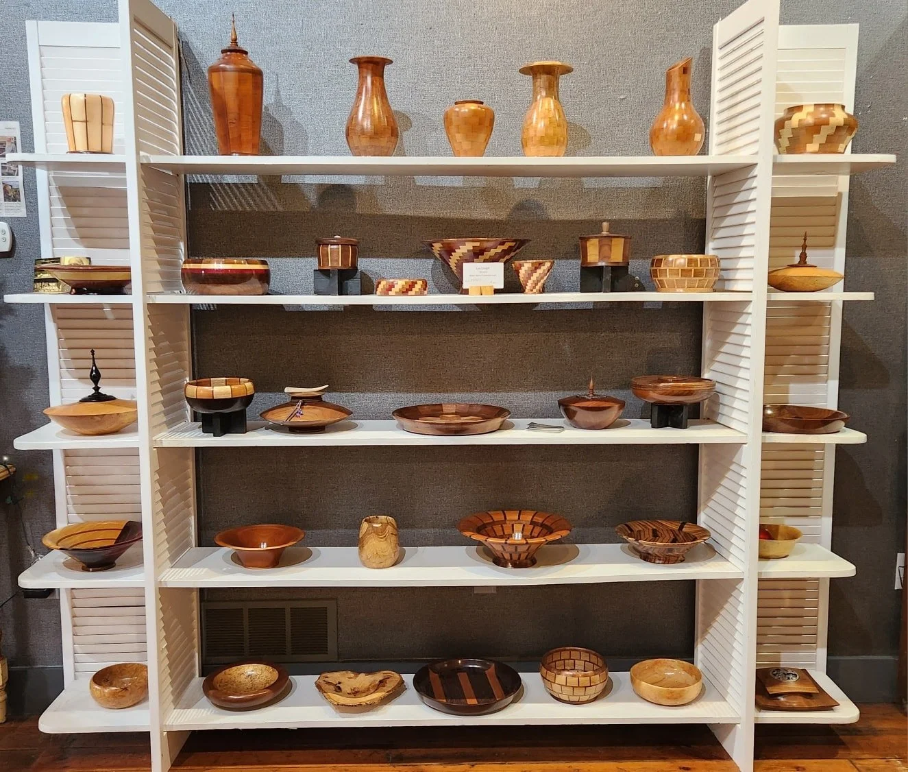 Wooden bowls and vases displayed on white shelves in an art gallery.