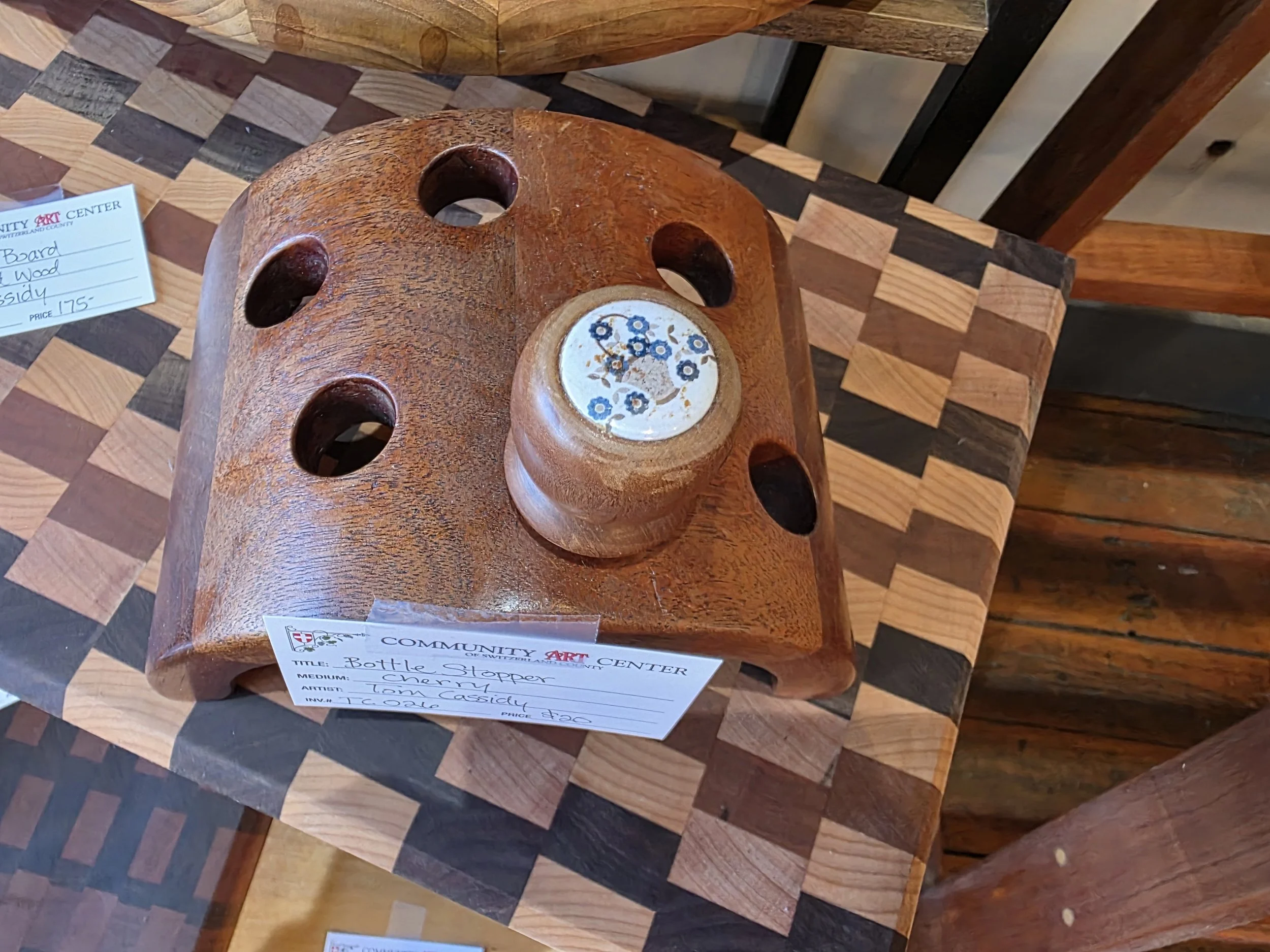Wooden bottle stopper with a chip decorated with blue flowers, displayed on a checkered wooden table.