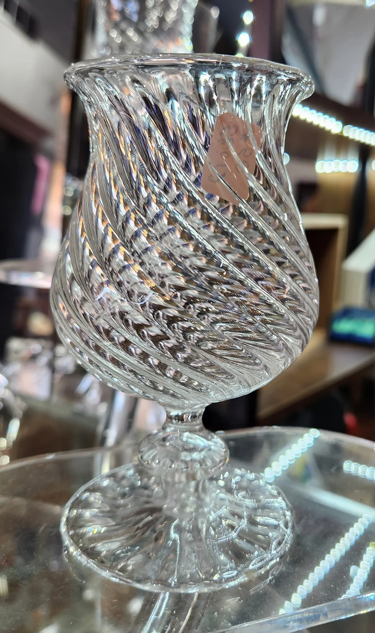 Clear cut glass vase with a twisted spiral design, displayed on a glass surface in a store.