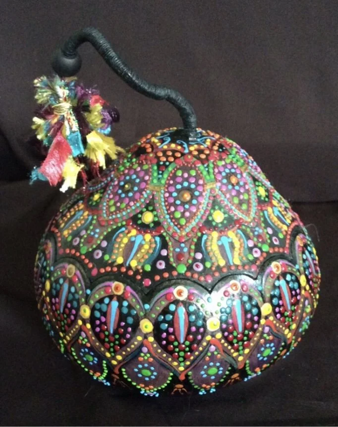 Decorative spherical object with intricate, colorful dotted patterns and a black stem with multicolored frayed fabric tassels, set against a black background.