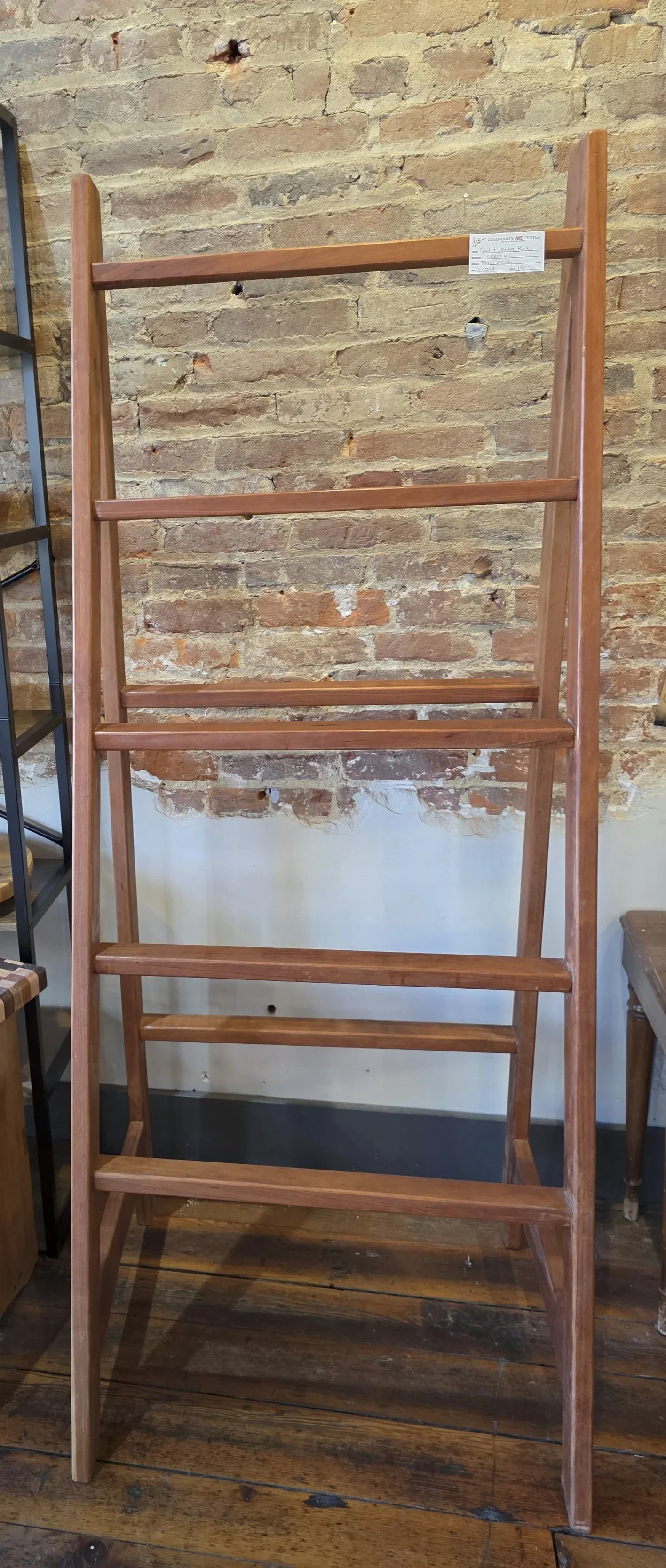 A wooden ladder rack with four shelves against a brick wall.