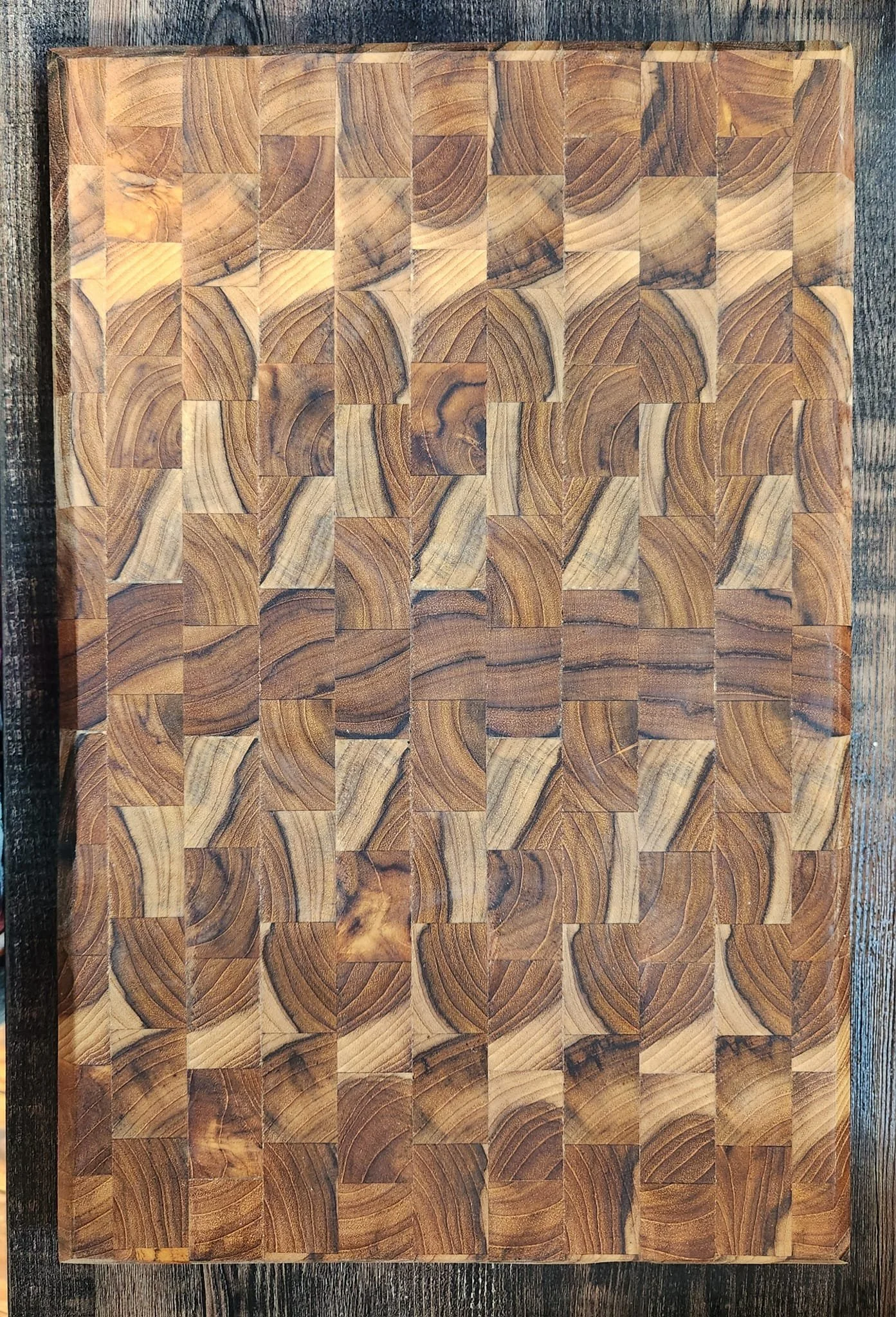 A wooden cutting board made of small, square wooden tiles arranged in a pattern, placed on a wooden surface.