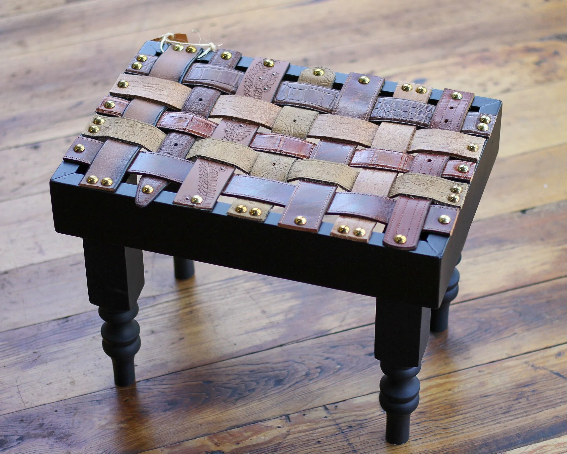 Small black table with a woven leather strap design on top, placed on a wooden floor.