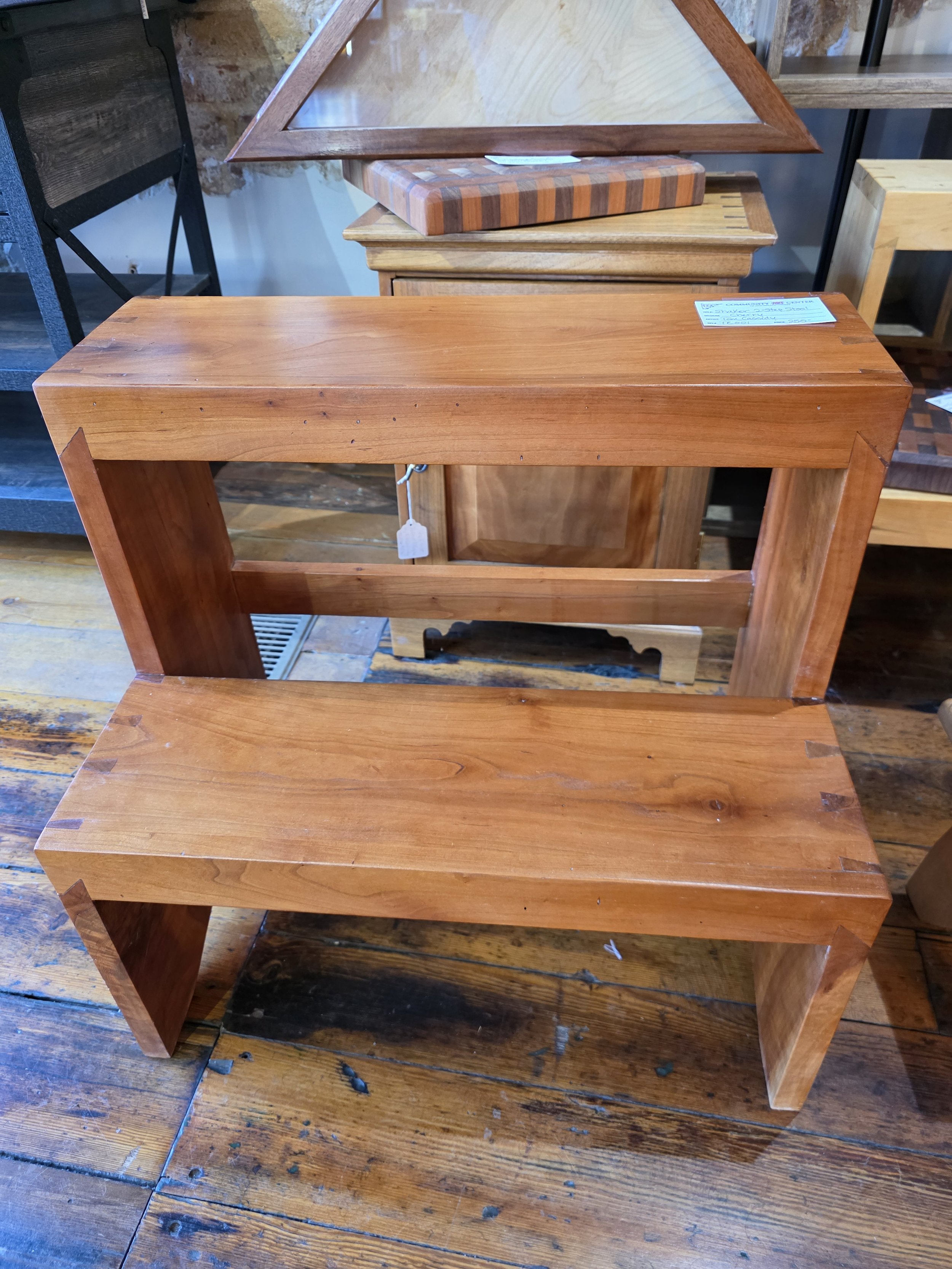 Unfinished wooden bench with a simple design, placed on a wooden floor in a store or workshop.