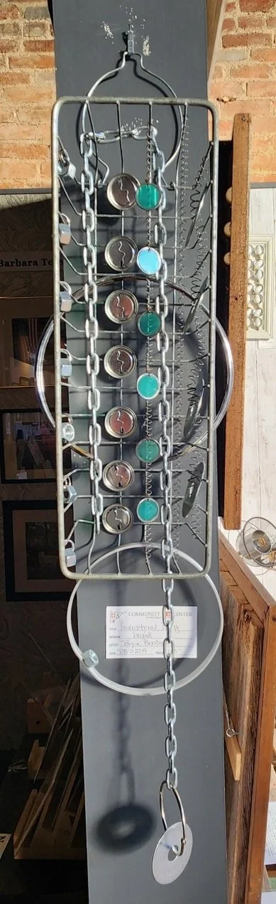 Metal museum exhibit featuring chains, gears, and circular objects on a vertical display board.