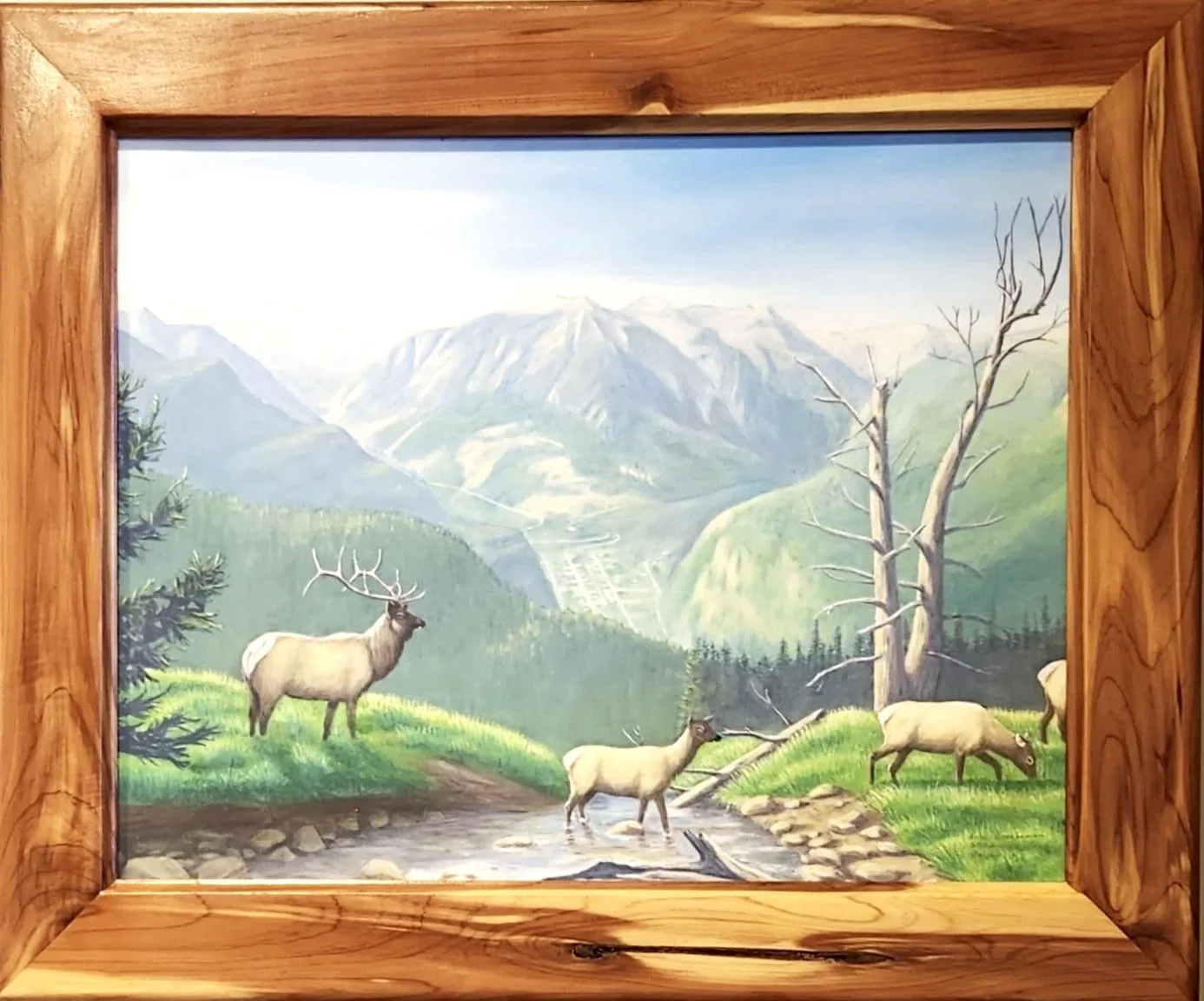 A painting of a mountain landscape with elk and a creek, framed in wood.