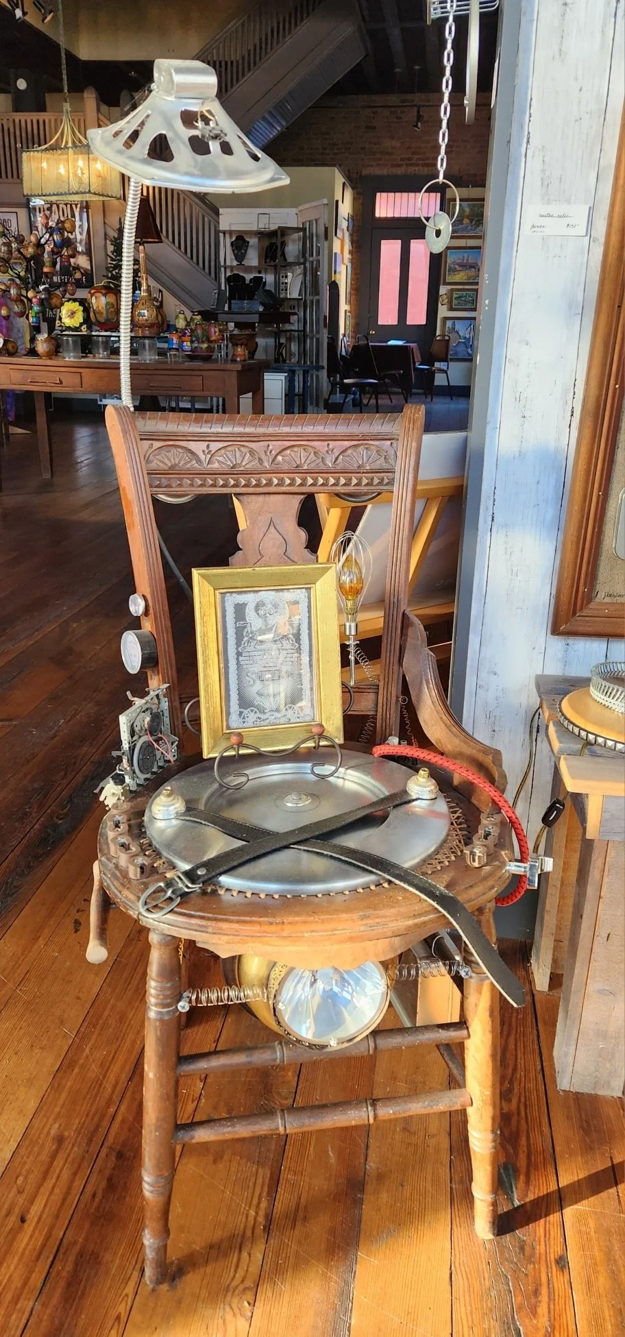 An eclectic assortment of vintage and steampunk objects on an old wooden chair, including a framed picture, a light bulb, and various small mechanical parts, in a cozy antique shop.