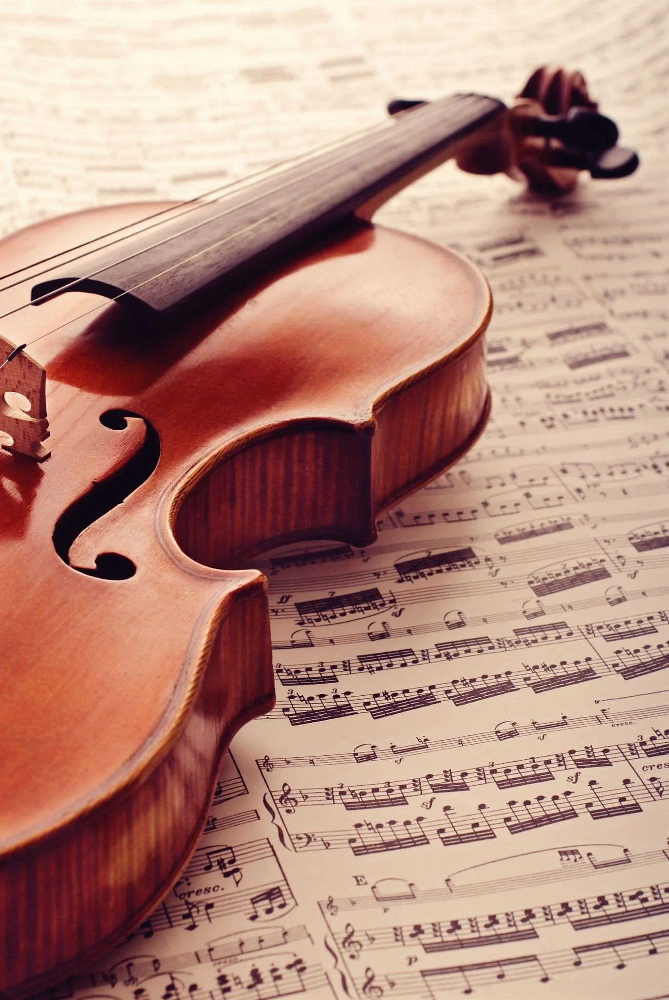 A wooden violin resting on sheet music filled with musical notes.