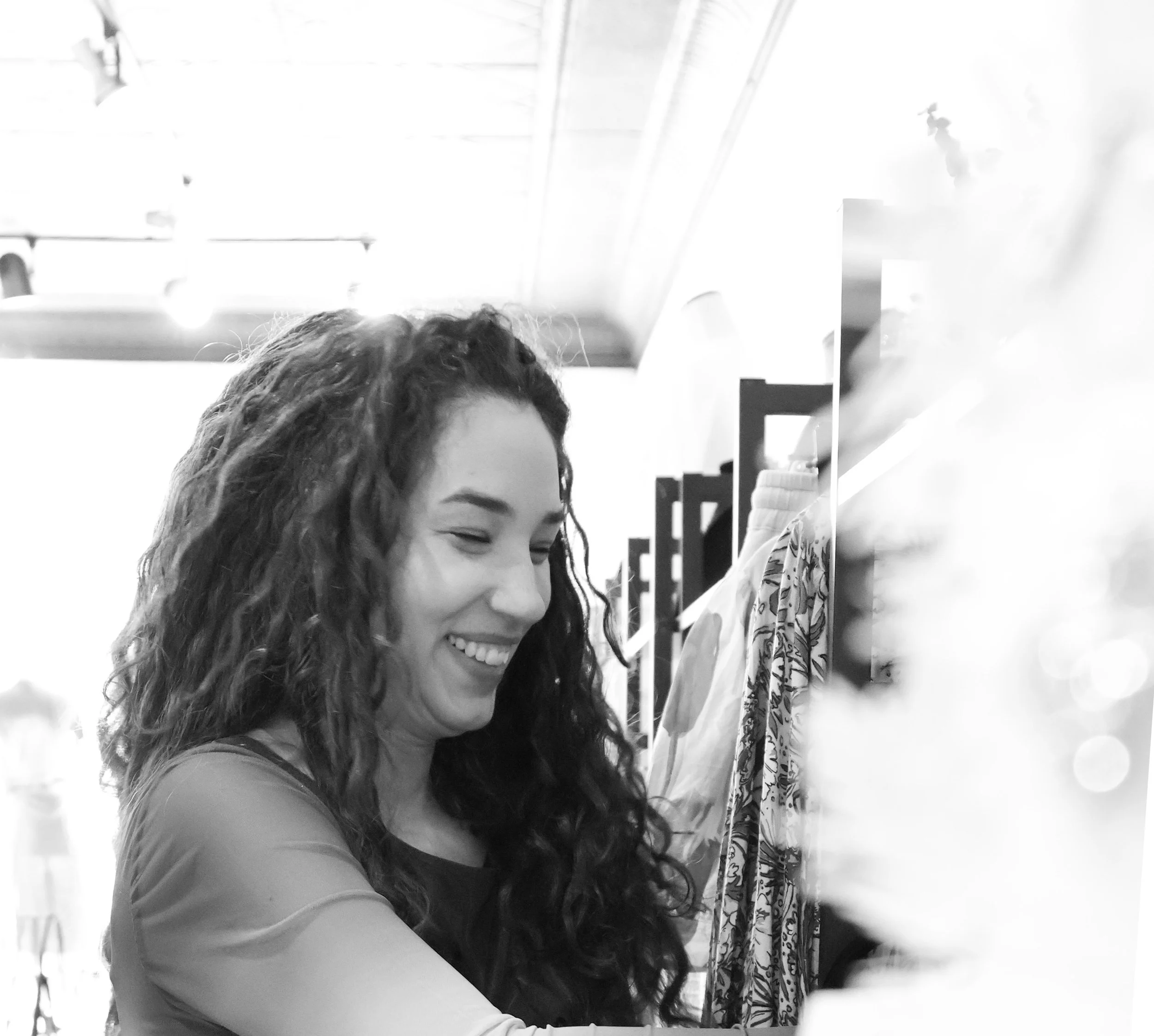 A woman with long, curly hair smiling while shopping for clothes in a store.