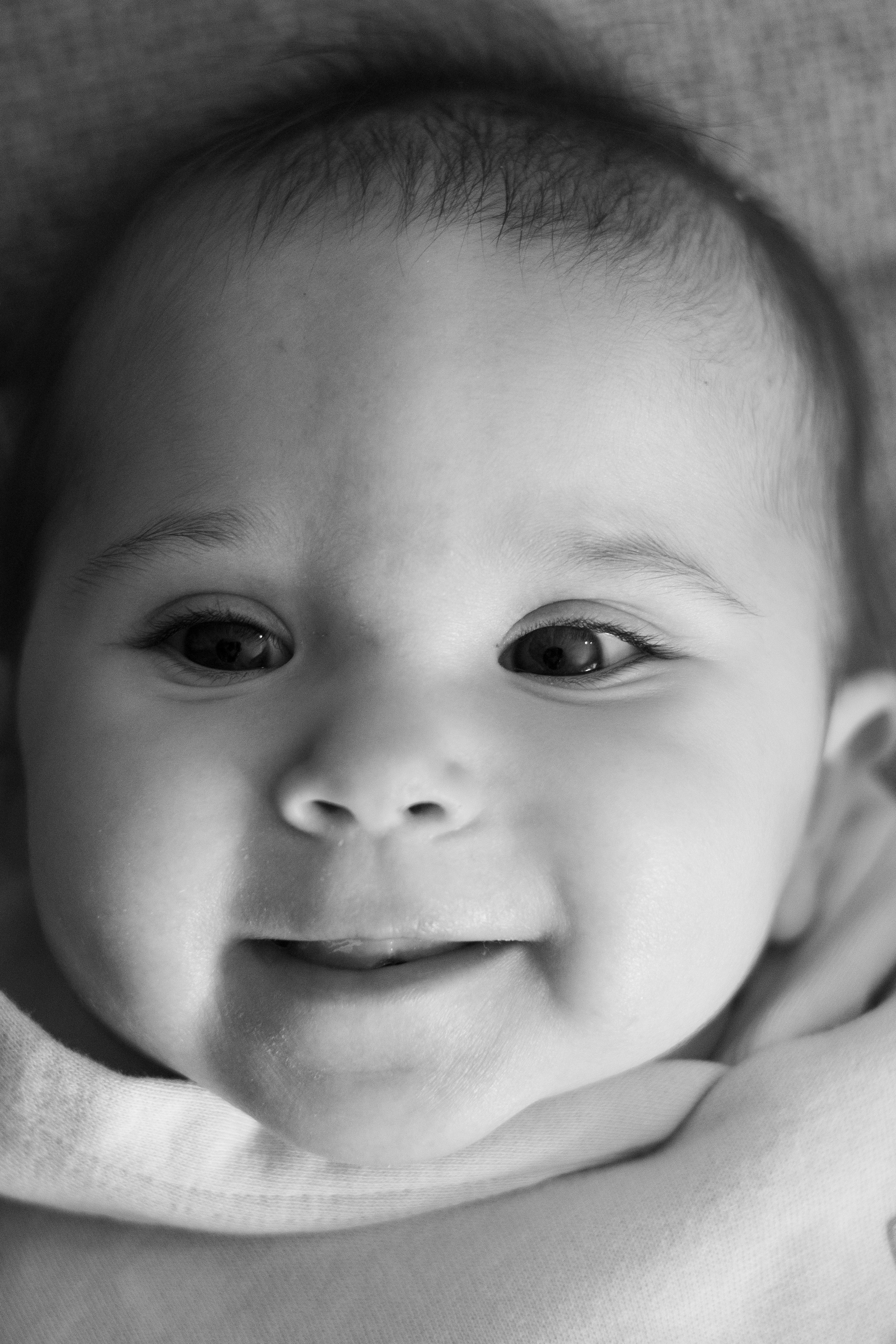 Close-up of a smiling baby's face in black and white, showing eyes, nose, and mouth.