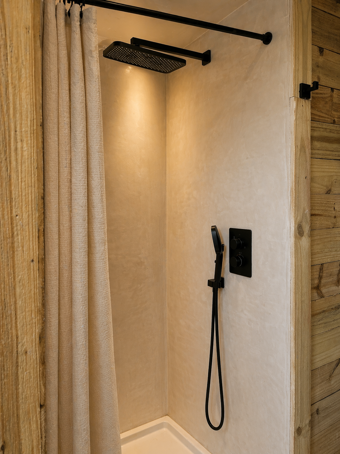 Shower with black rainfall showerhead, handheld shower, beige wall, wooden wall, and beige curtain.