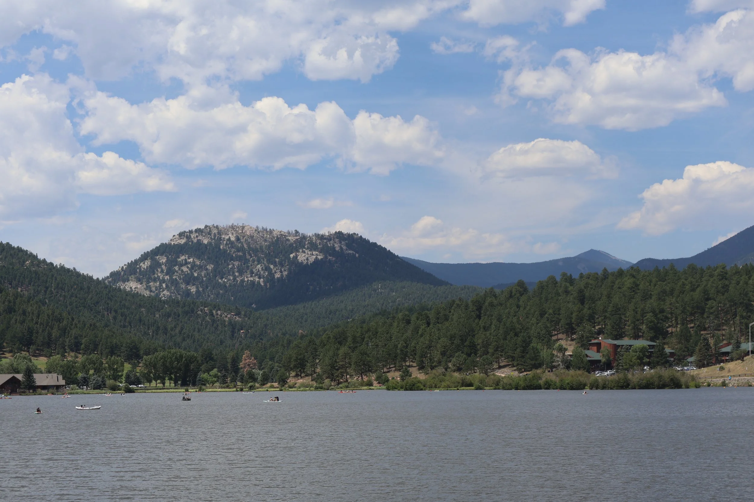 Mountain lake surrounded by dense evergreen trees under a partly cloudy sky.