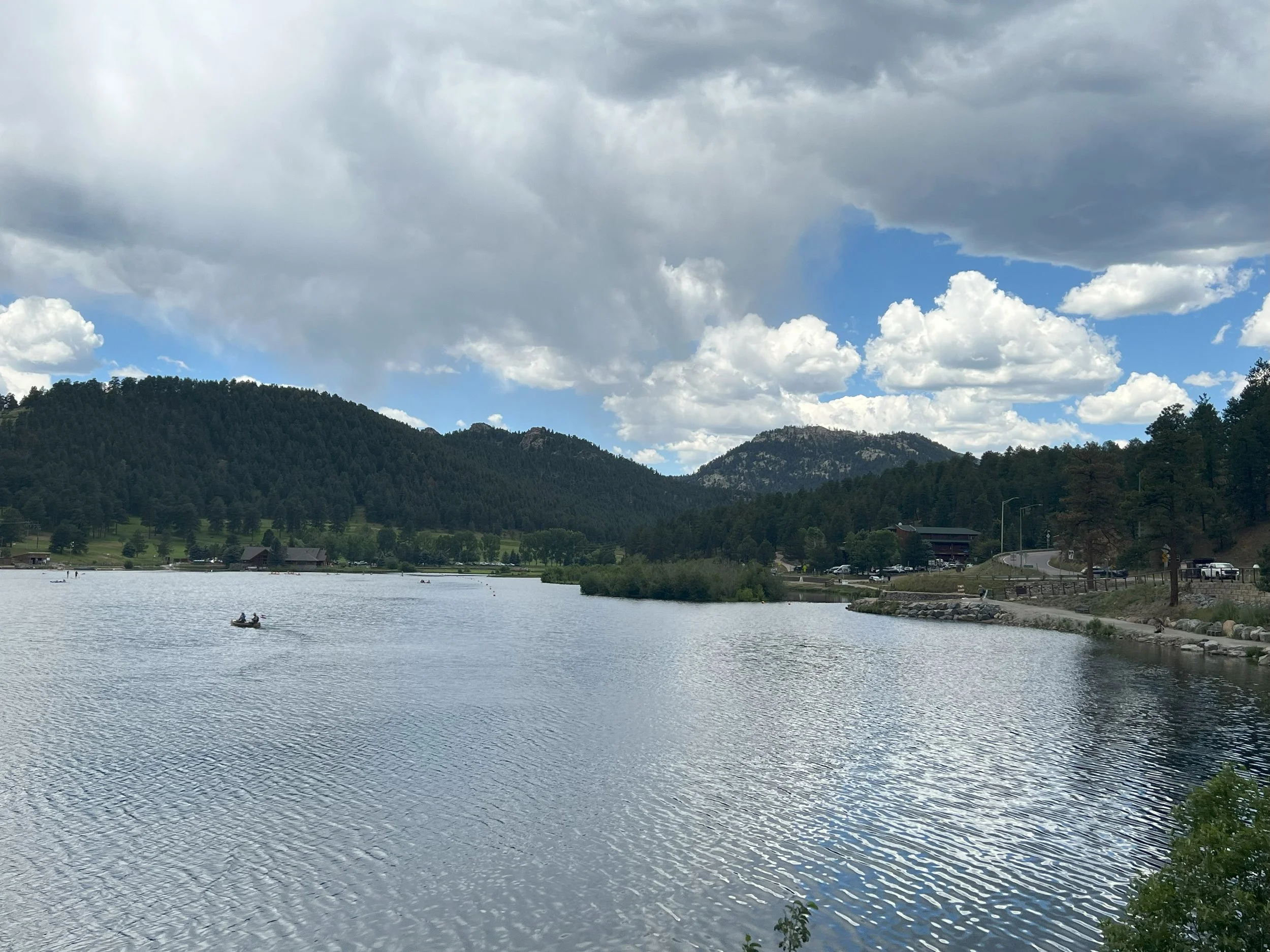 Scenic view of a lake with mountains and hills in the background, partly cloudy sky, and a boat with two people on the water.