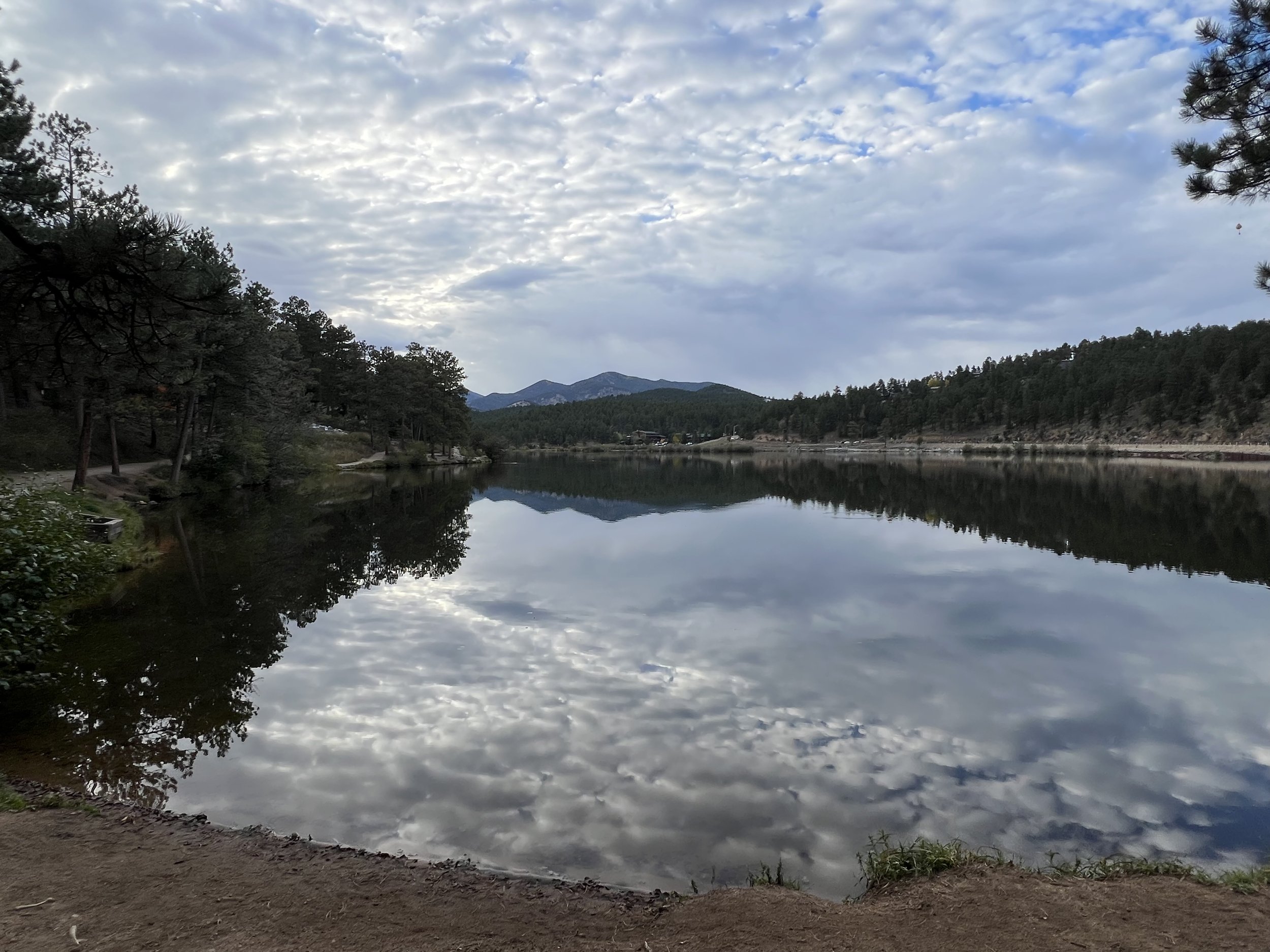 A calm lake reflecting the cloudy sky and surrounding forested hills