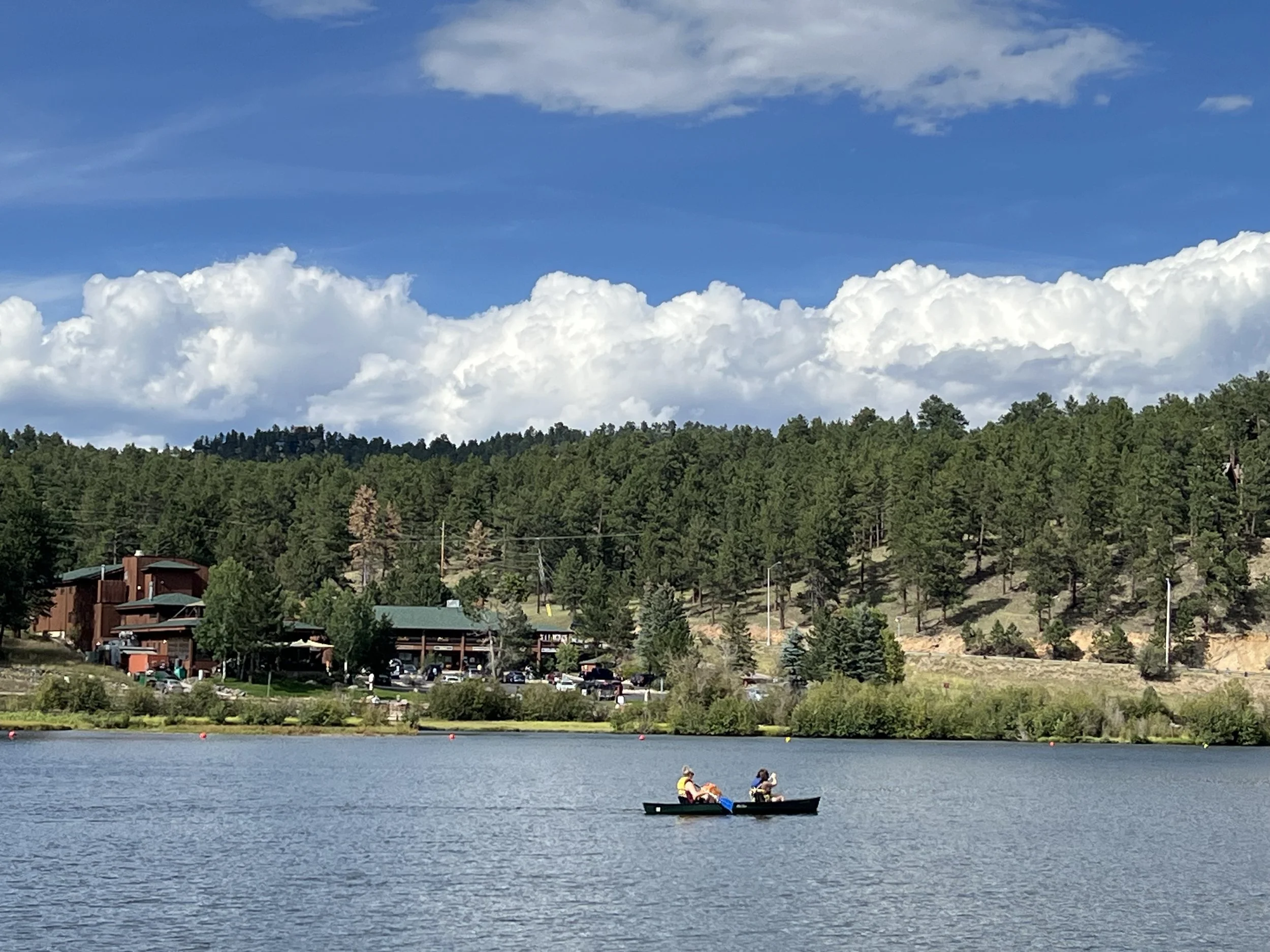 People in a canoe on a lake with a forested hillside and partly cloudy sky in the background.