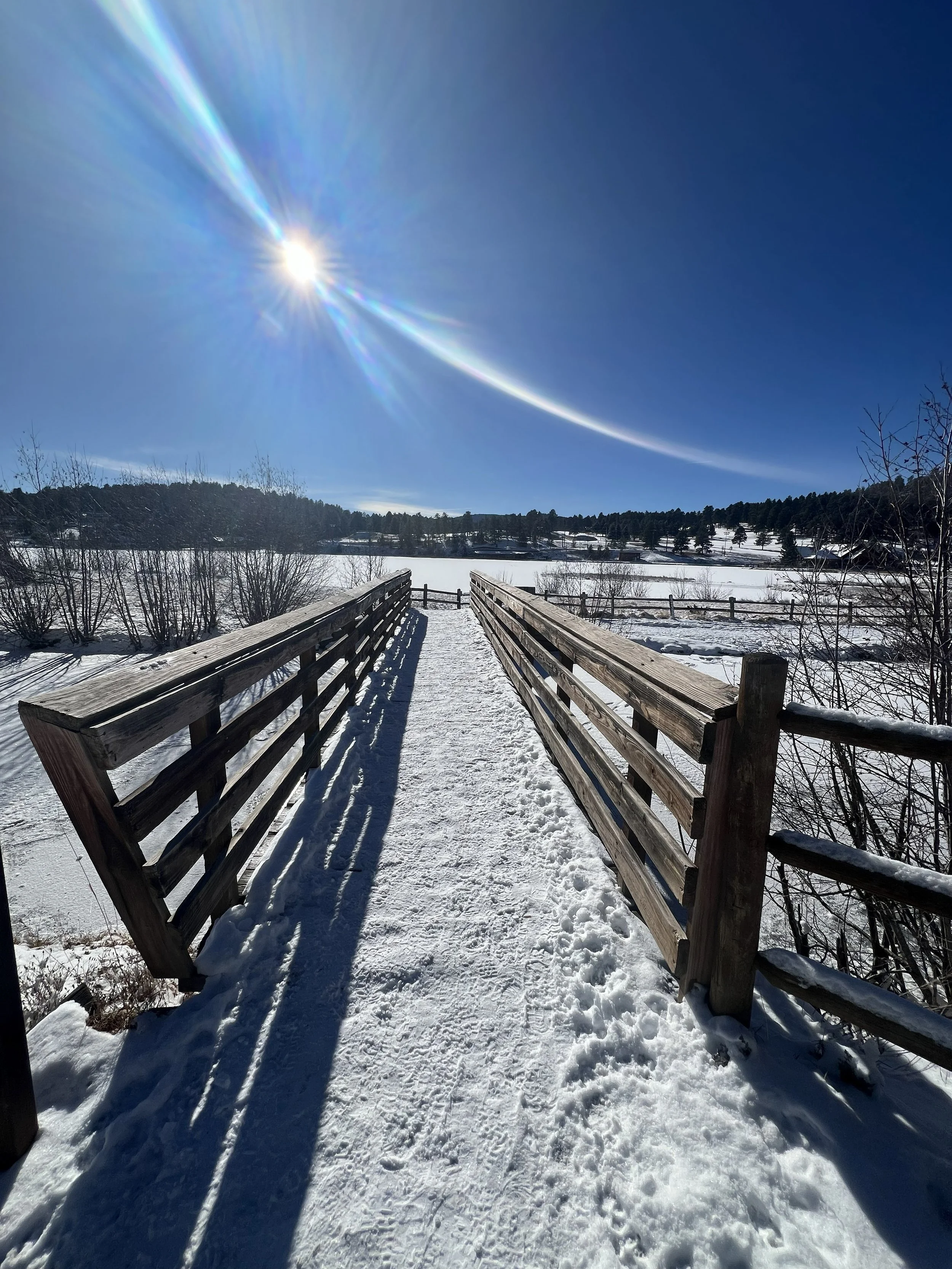 Snow-covered bridge over a frozen river under a clear blue sky with the sun shining brightly.