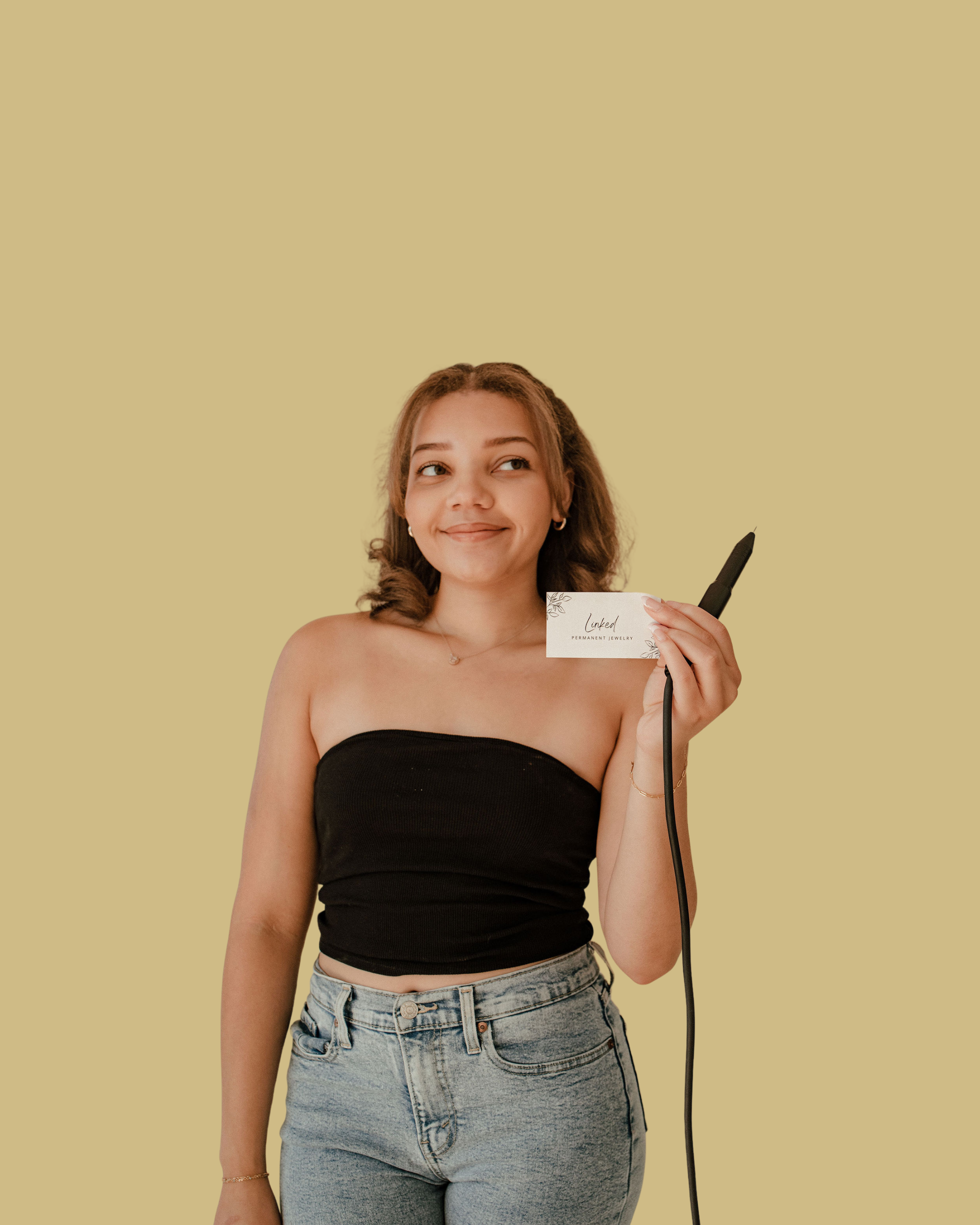 Jayda is standing wearing a black tube top and holding her business card and welding pen