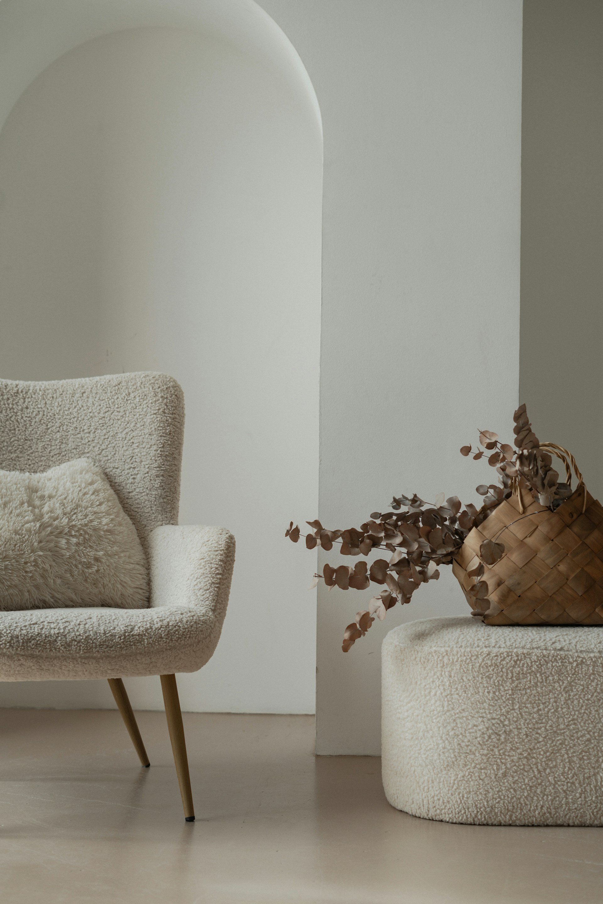 Sillón de textura suave beige con cojín de peluche y recipiente de mimbre con ramas secas en un espacio minimalista