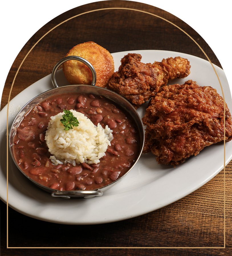 Fried chicken leg, hush puppy, baked beans with mashed potatoes and parsley on a white plate.