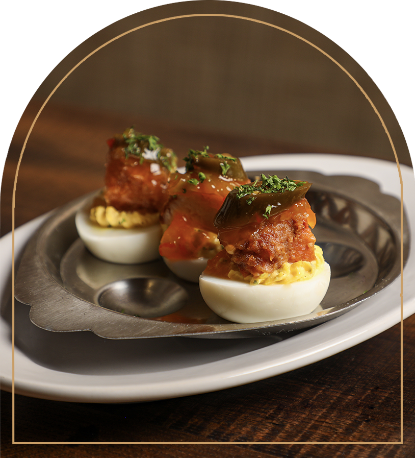 Deviled eggs topped with chopped herbs and a garnish of jalapeño slices on a metal serving tray.