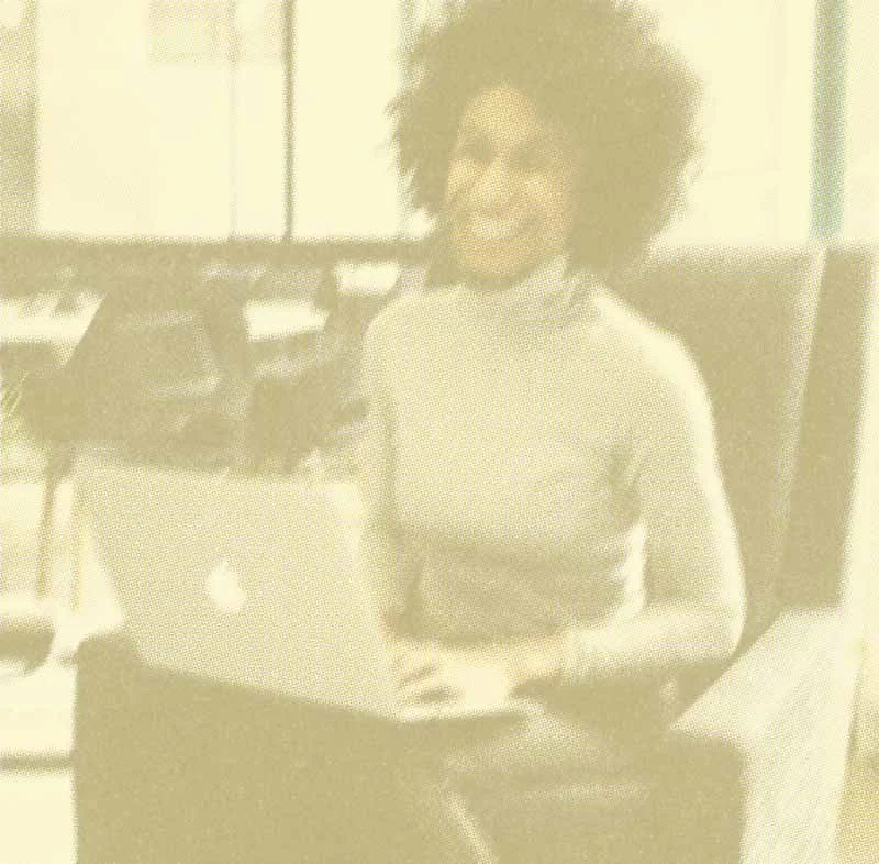 Woman with curly hair sitting at a desk with a laptop, smiling