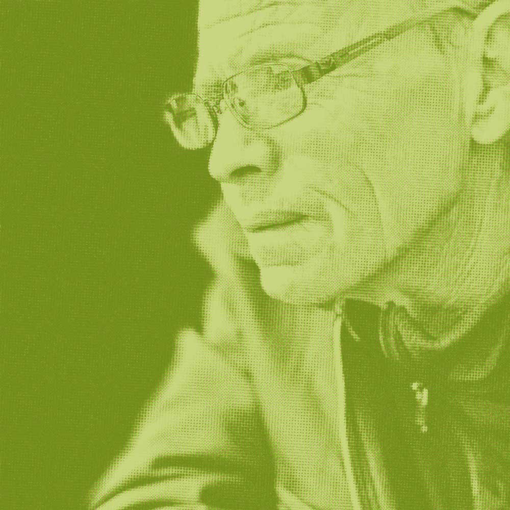 Close-up of an elderly man with eyeglasses smiling, with her hand resting on her cheek, wearing a jacket.