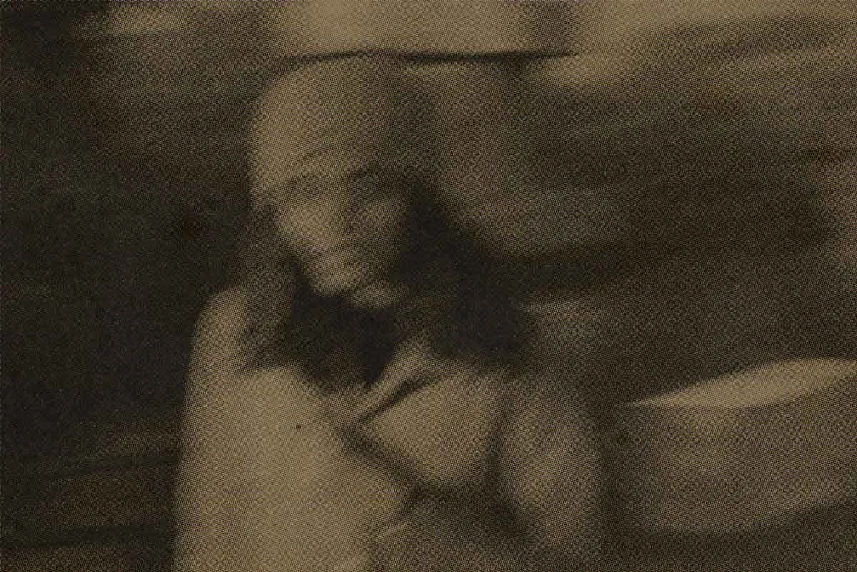 Faded, blurry image of a woman with long hair with a hat and coat, walking and looking at the camera.
