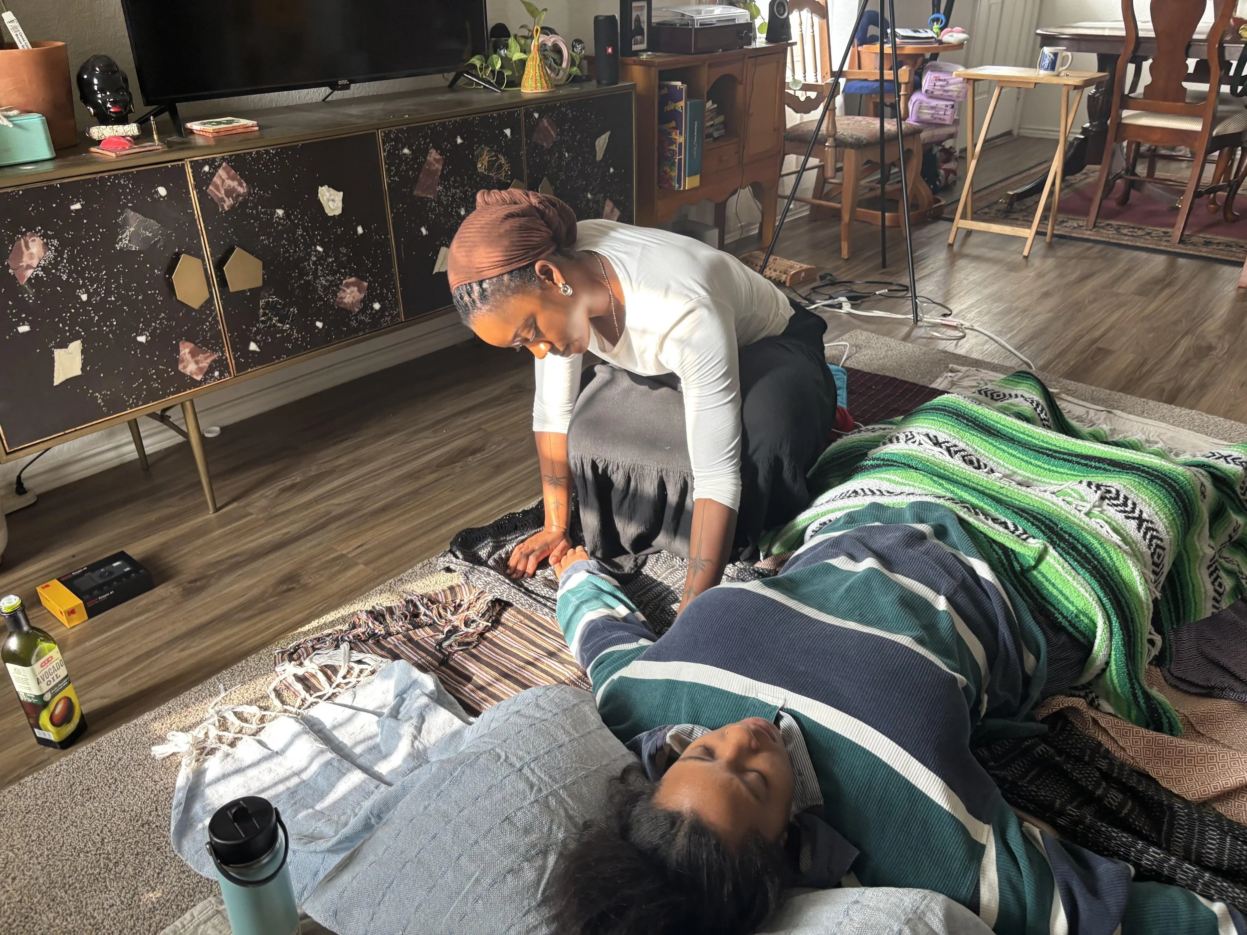 A woman performs a ceremonial cerrada on a woman lying on the floor in a living room.