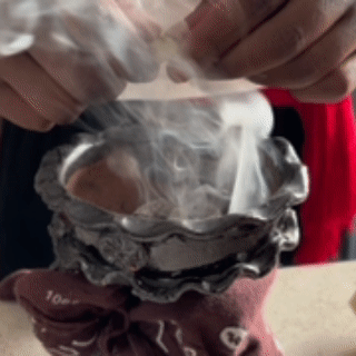 Hand holding a steaming, foil-wrapped dish or container.