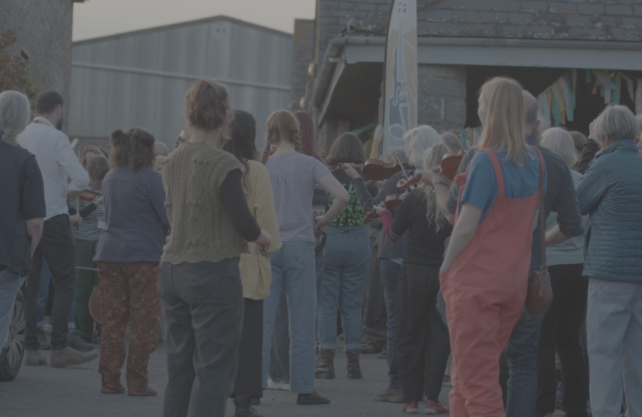 People gathered outdoors, some playing violins, at a community event or festival.