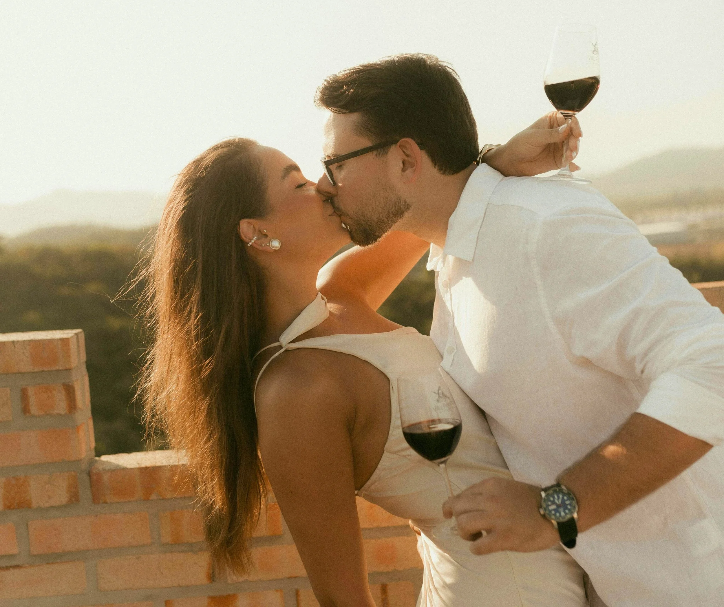 Un couple s'embrasse passionnément lors d'une soirée avec des verres de vin rouge à la main.