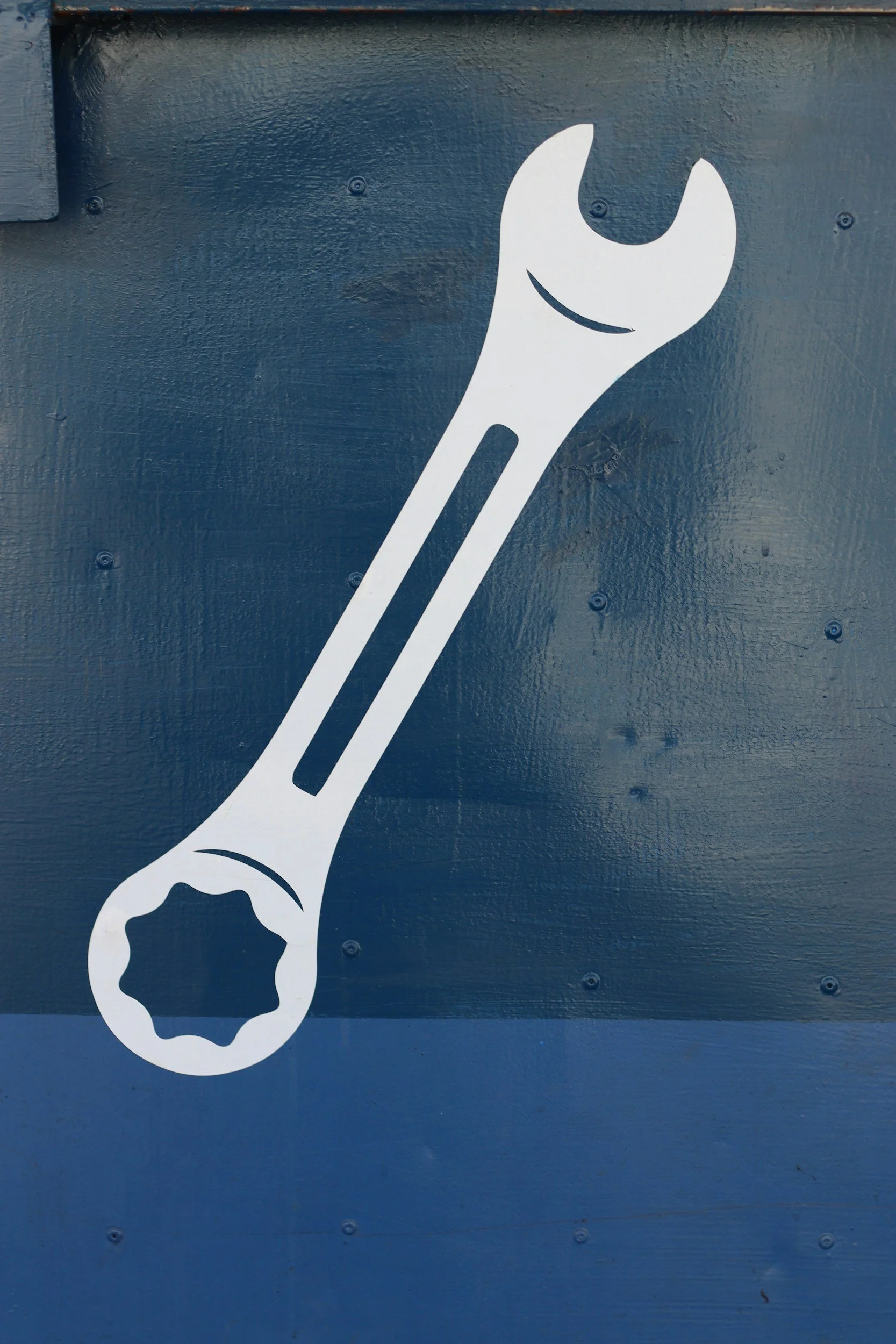 White sticker of a wrench with the handle forming the shape of a dog's paw, placed on a dark blue metal surface.
