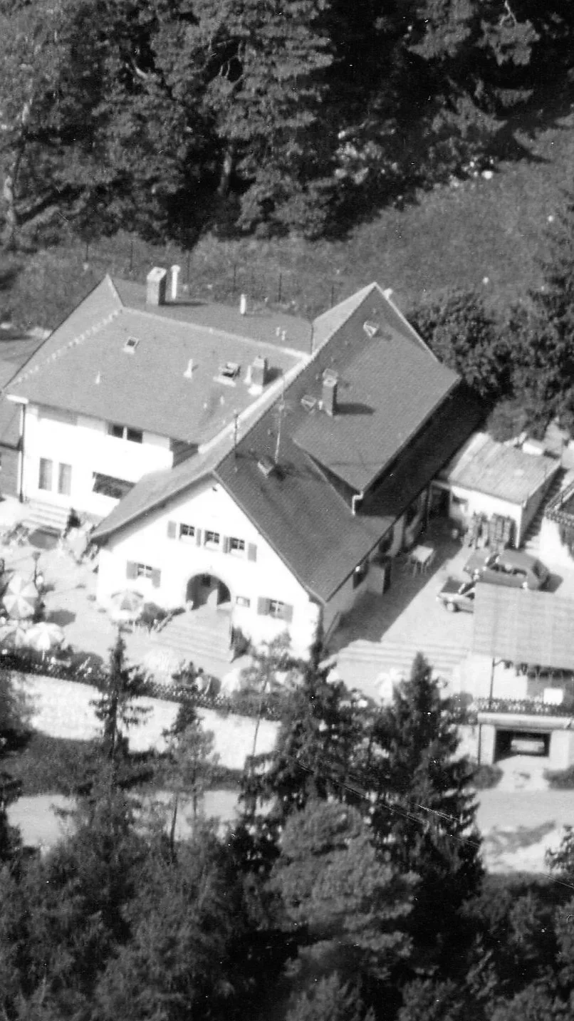 Luftaufnahme eines Hauses mit mehreren Dächern, umgeben von Bäumen und Gartenflächen.