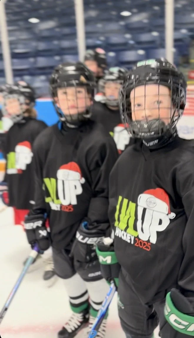 Hockey players in black jerseys with Christmas-themed logo, standing on ice rink.