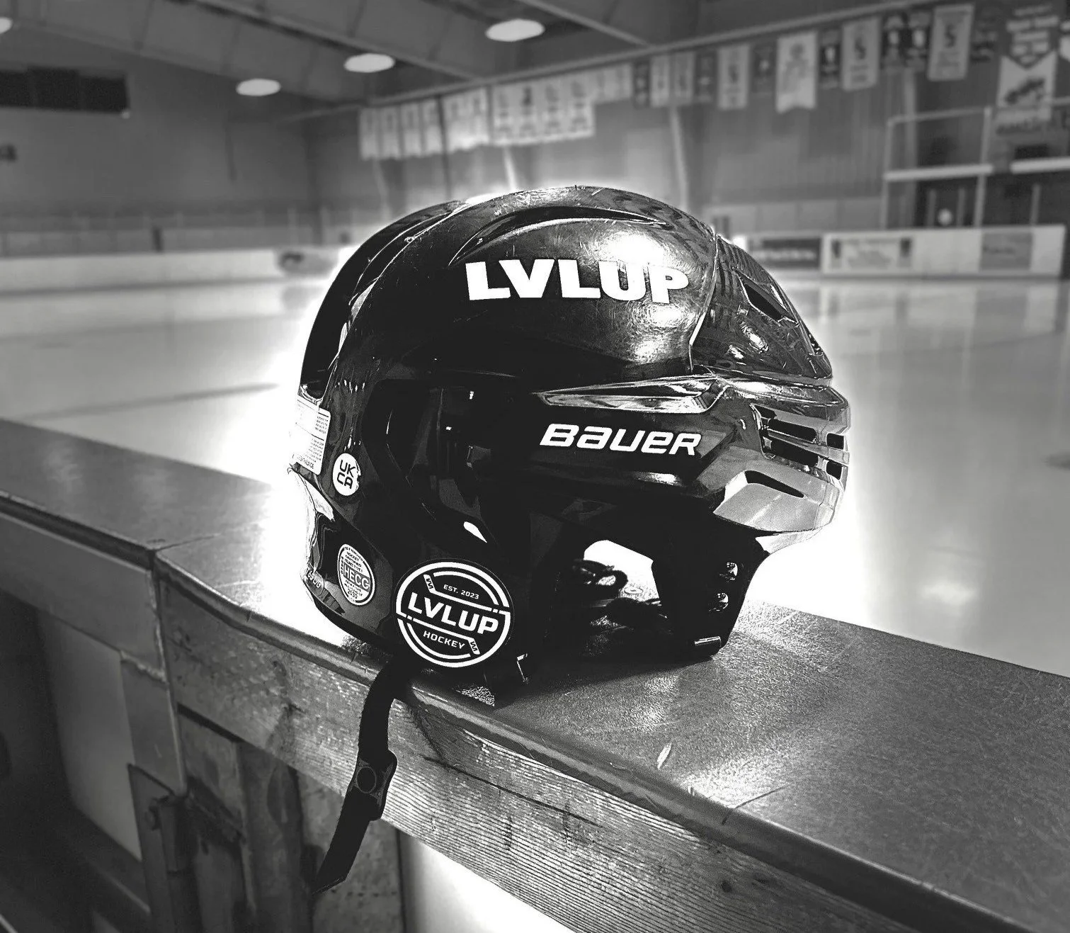 Black hockey helmet with stickers, placed on the edge of an ice rink with an empty ice surface in the background.