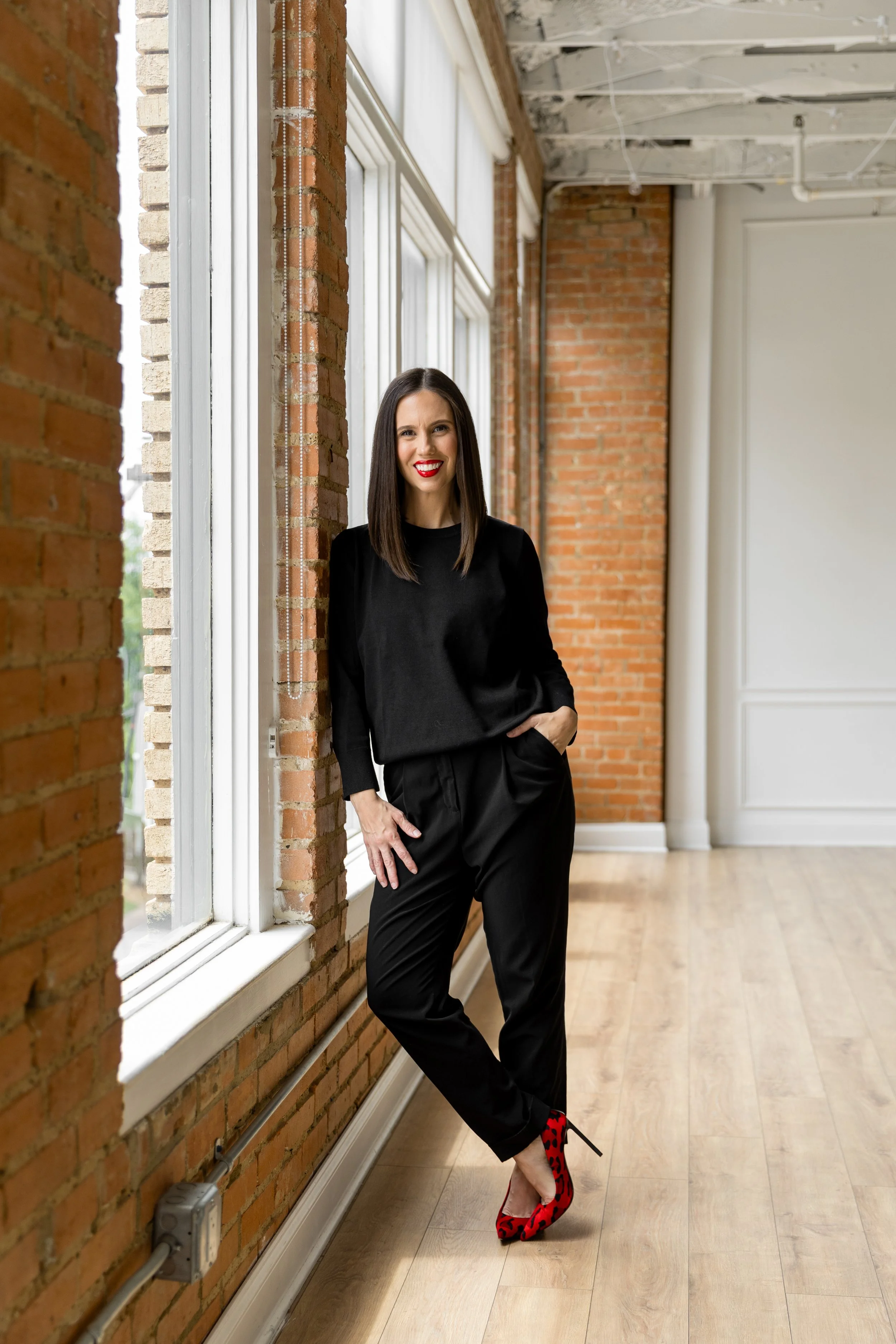 Debut author Whitney Cummins in a sunlit loft studio, dressed in black with red heels