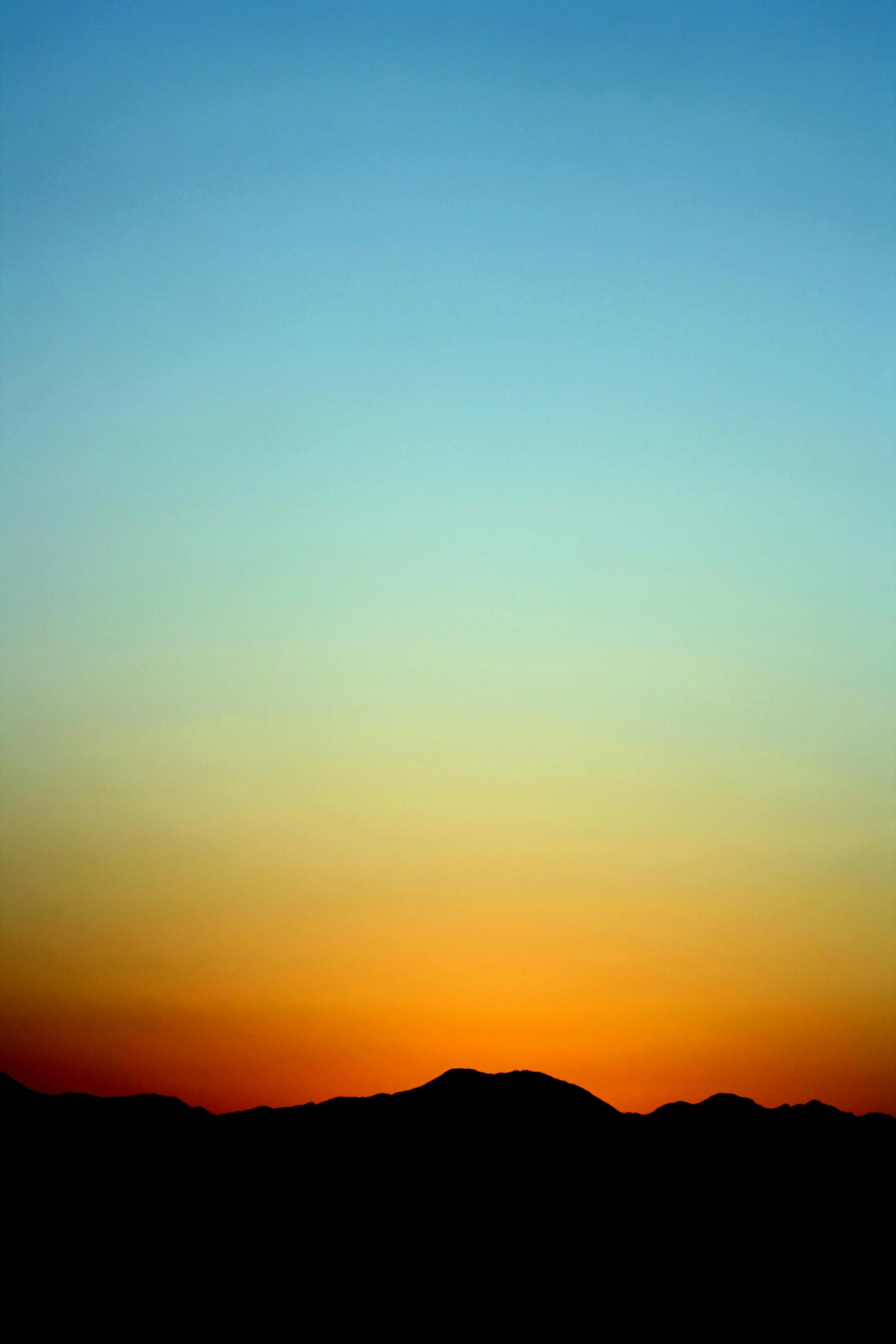 Sunset over mountains with colorful sky, transitioning from blue to orange and red hues.