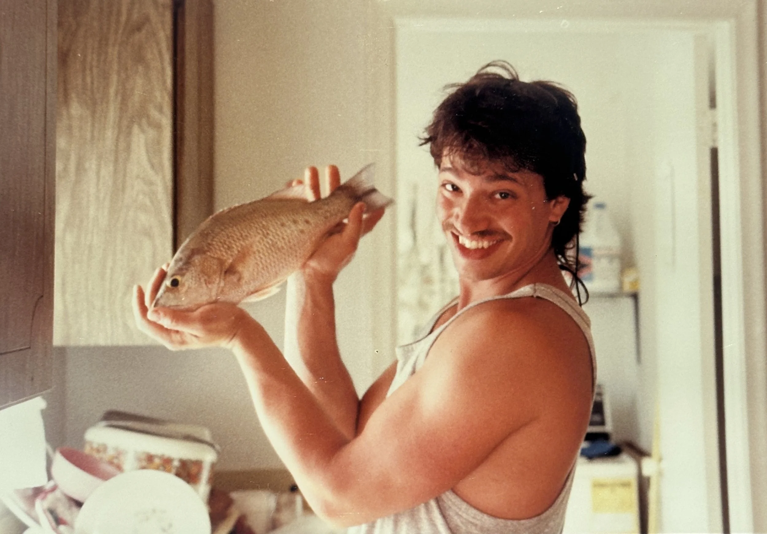 A woman with short dark hair holding a fish in a kitchen.