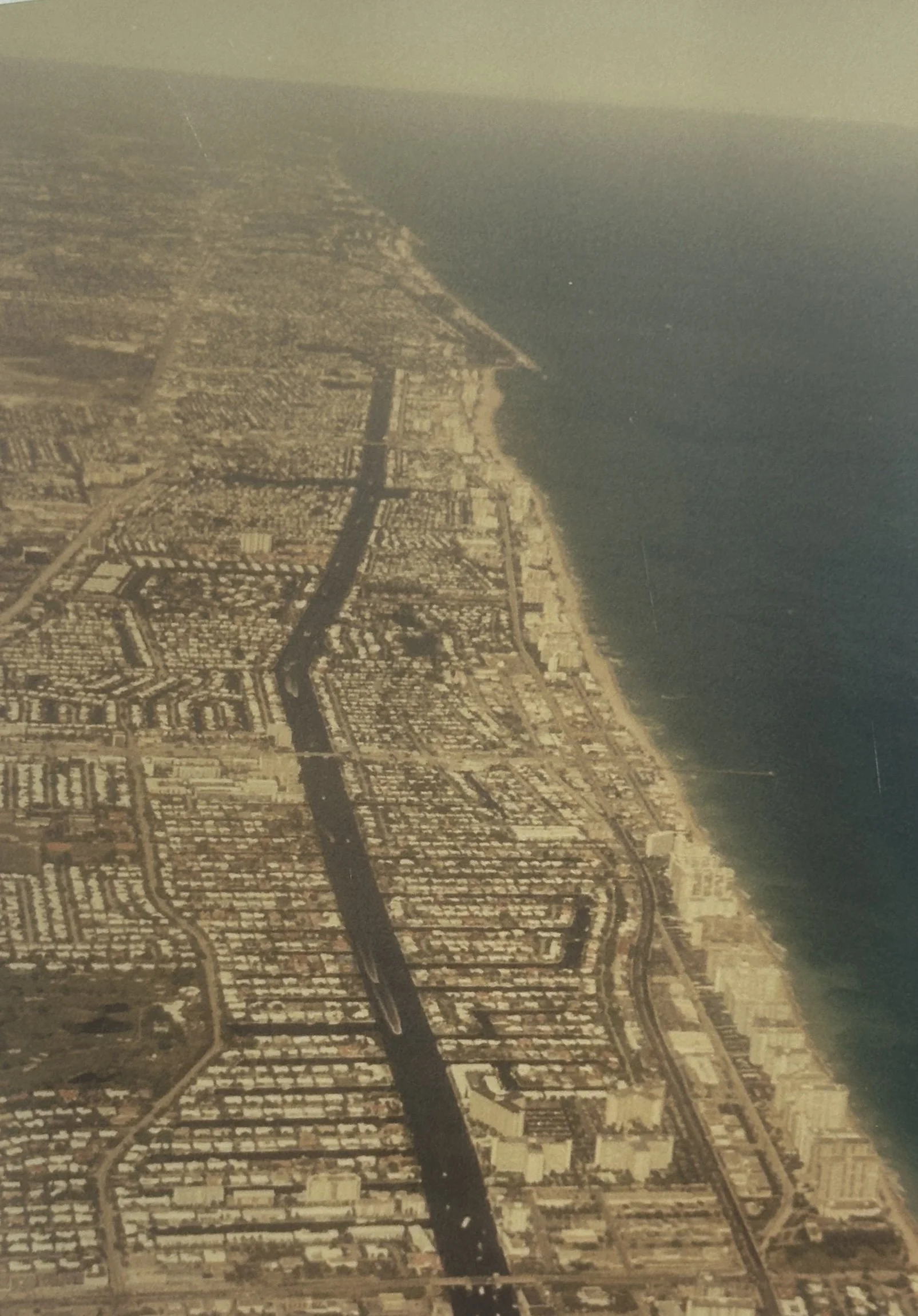 Aerial view of a coastal city with streets, buildings, and a large body of water along the shoreline.