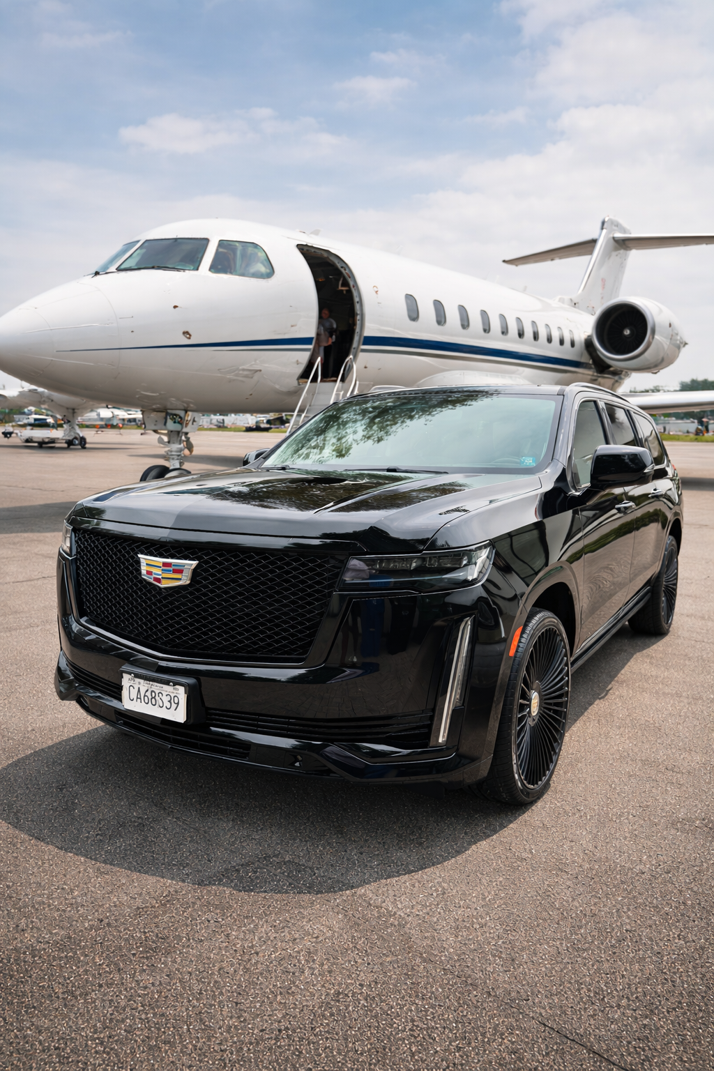 Black Cadillac SUV parked on tarmac in front of a private jet airplane.