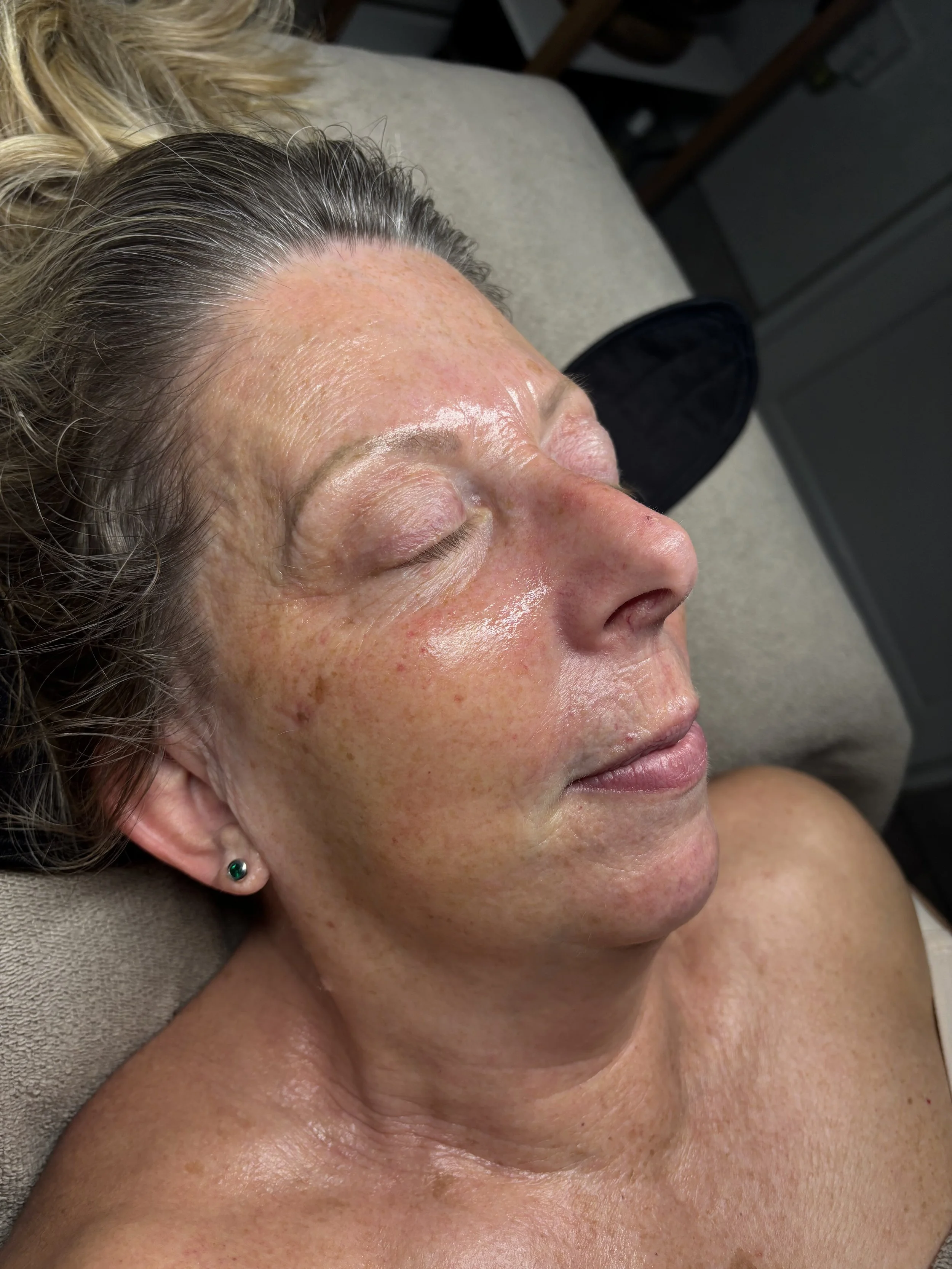 Close-up of a woman with her eyes closed, lying on a surface, showing her face and upper body with a natural complexion, in a relaxed setting.