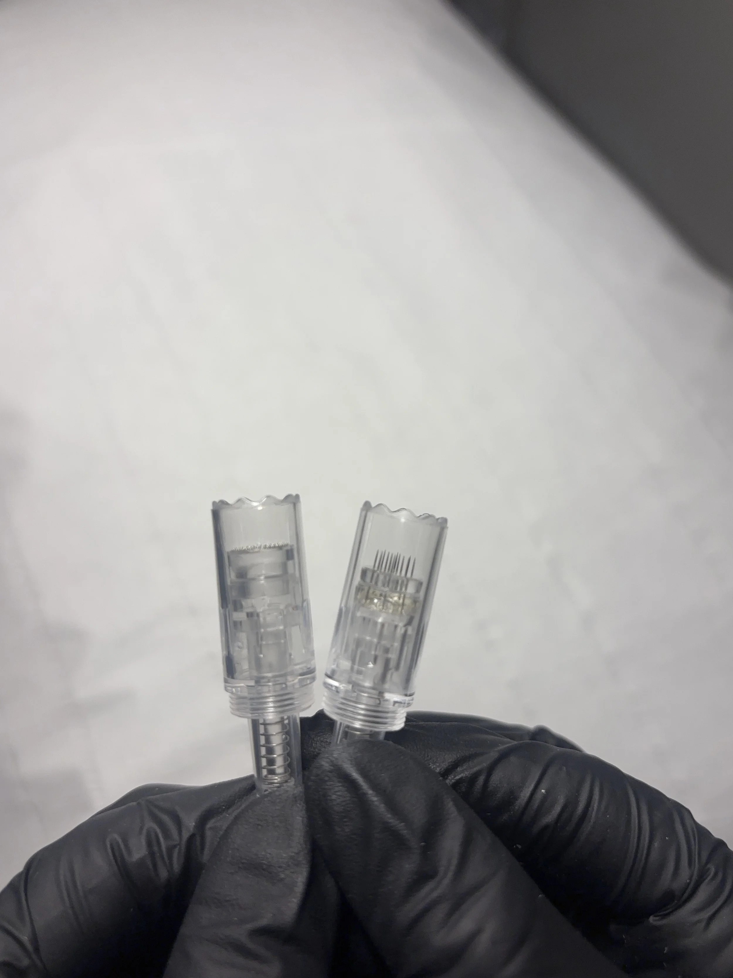 A person wearing black gloves holds three clear plastic spray bottles with barcodes against a plain white background.