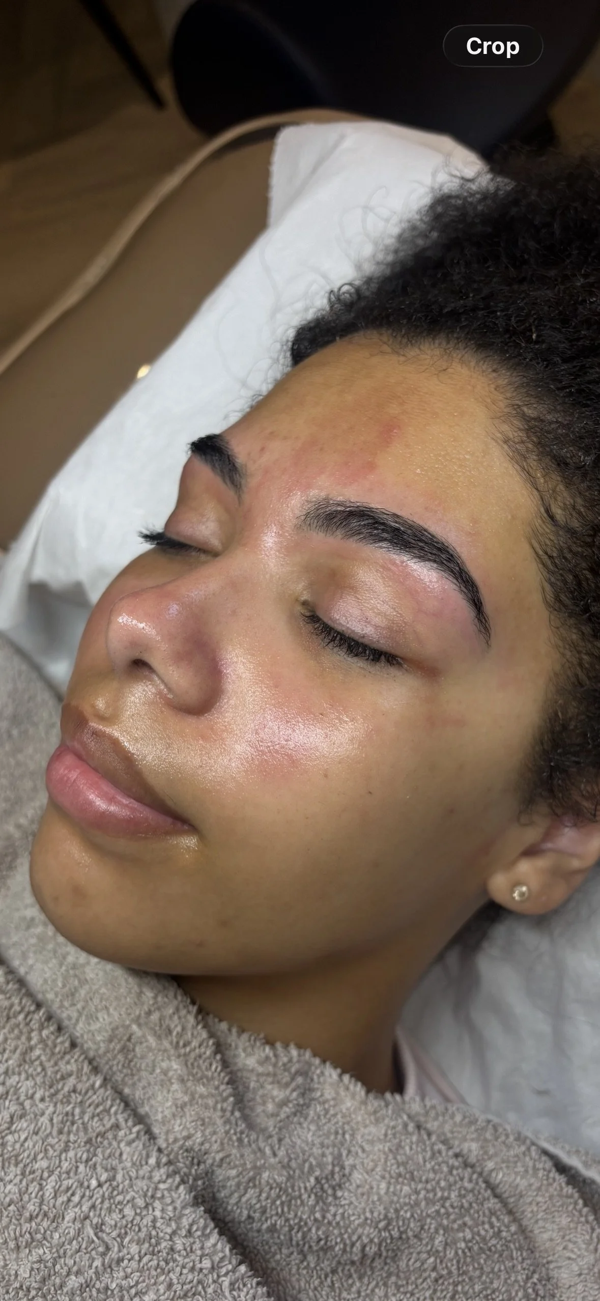A woman has her eyes closed while lying down, showing her freshly done eyebrows. She is relaxing with a peaceful expression.