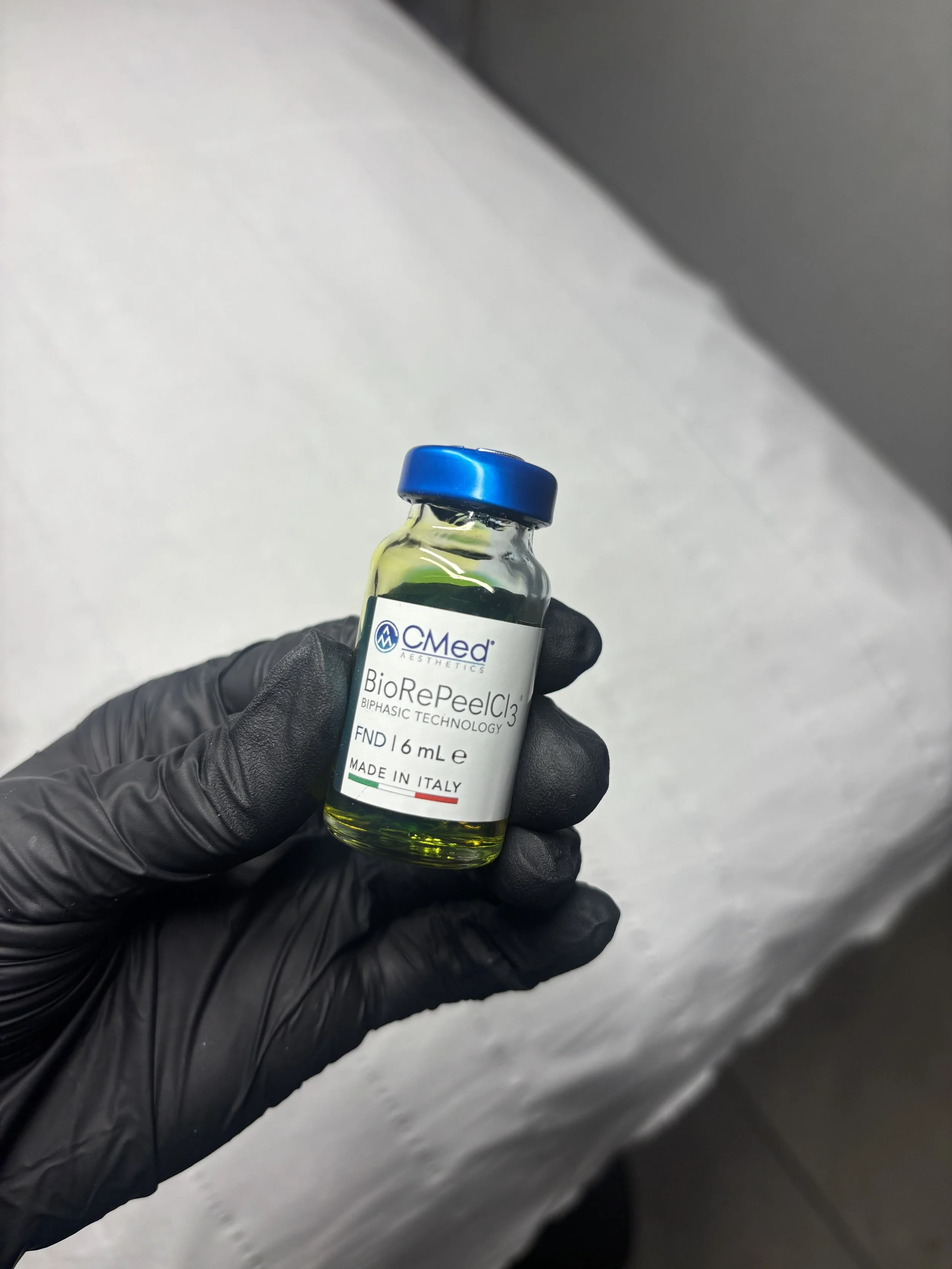 Small vial of BioRePeelCl3 solution held by a gloved hand against a plain background.