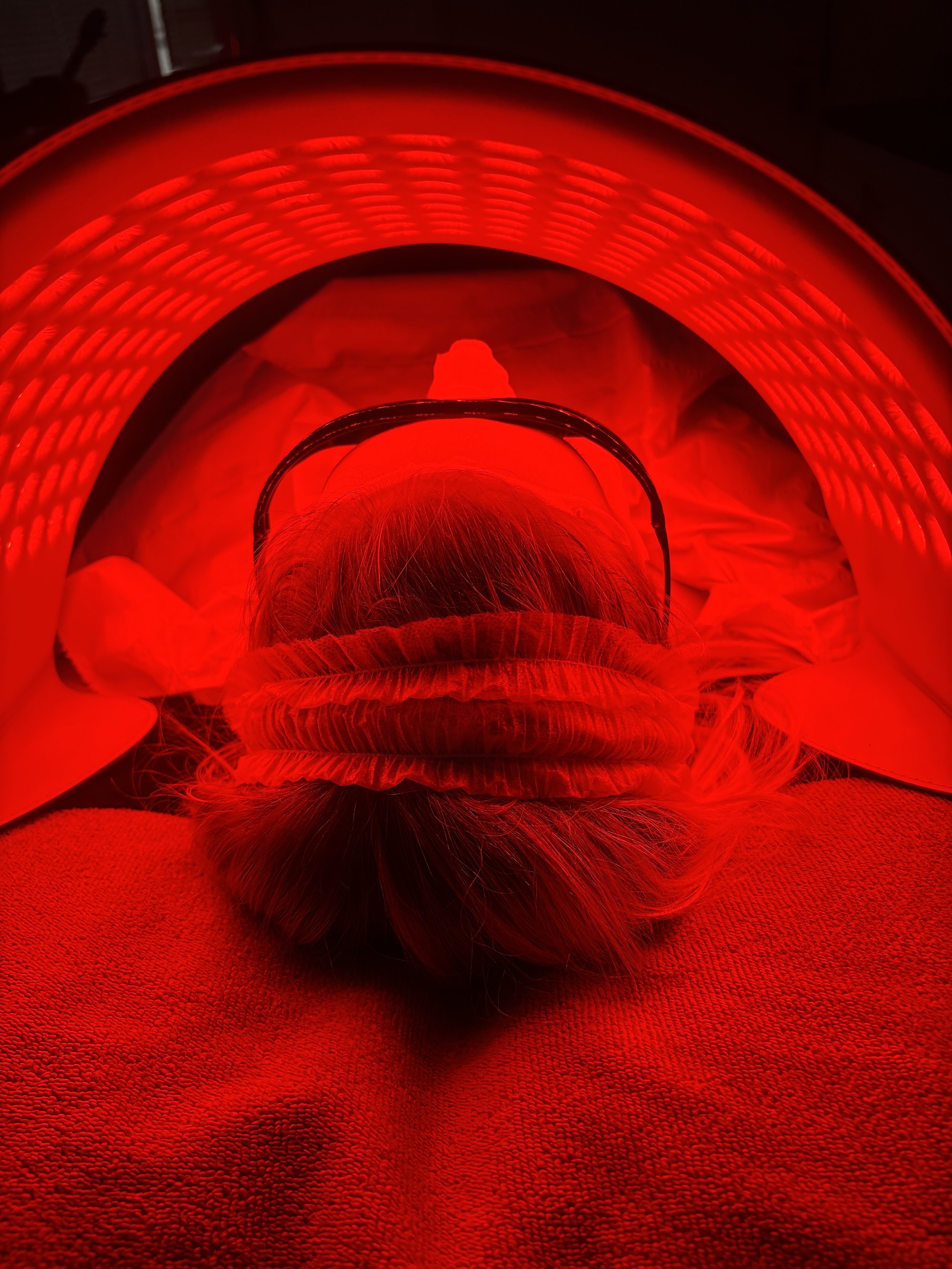Person lying down under red UV light cap, with hair, head, and pillow visible.