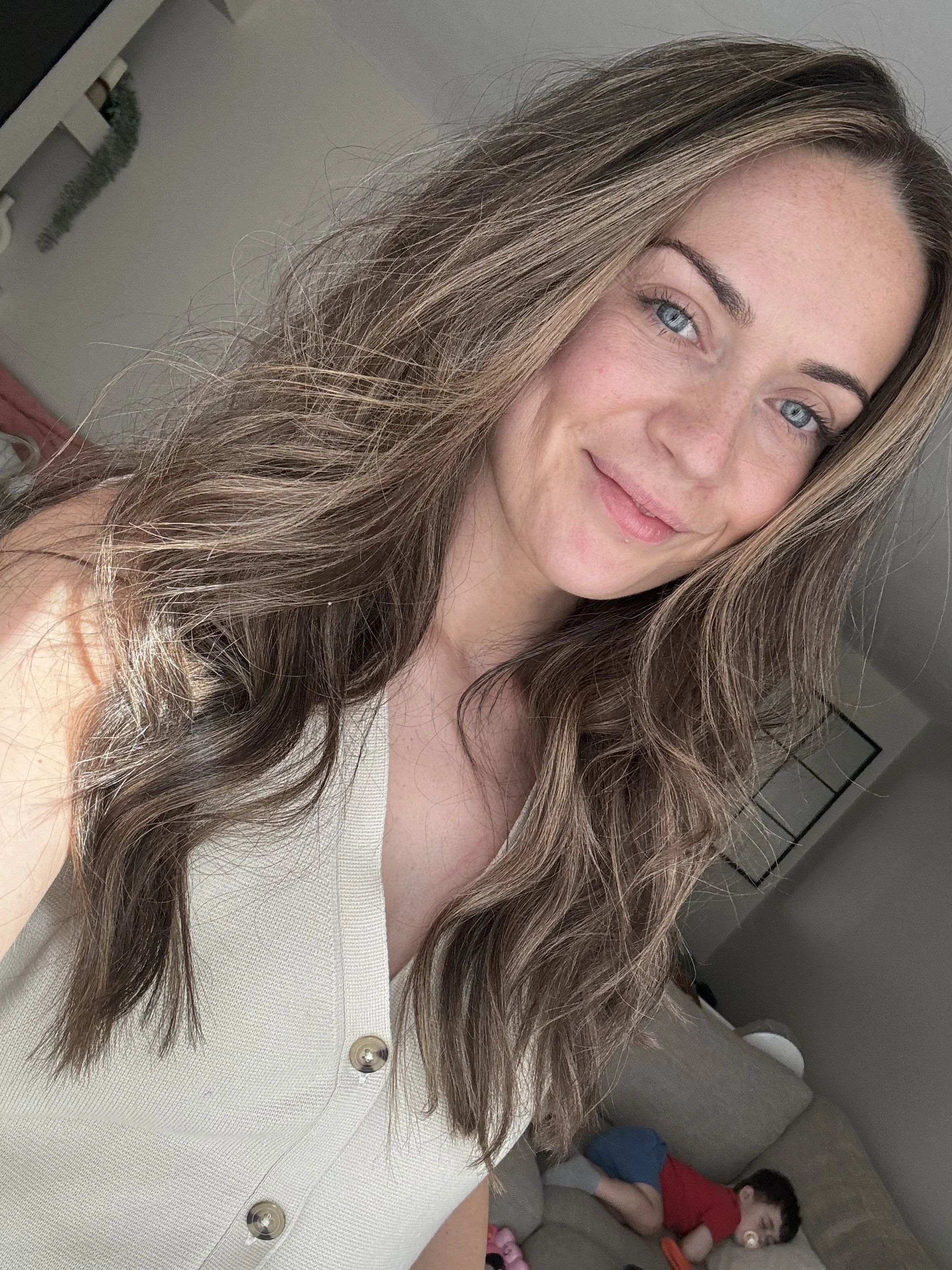 A woman with long wavy brown hair and blue eyes taking a selfie