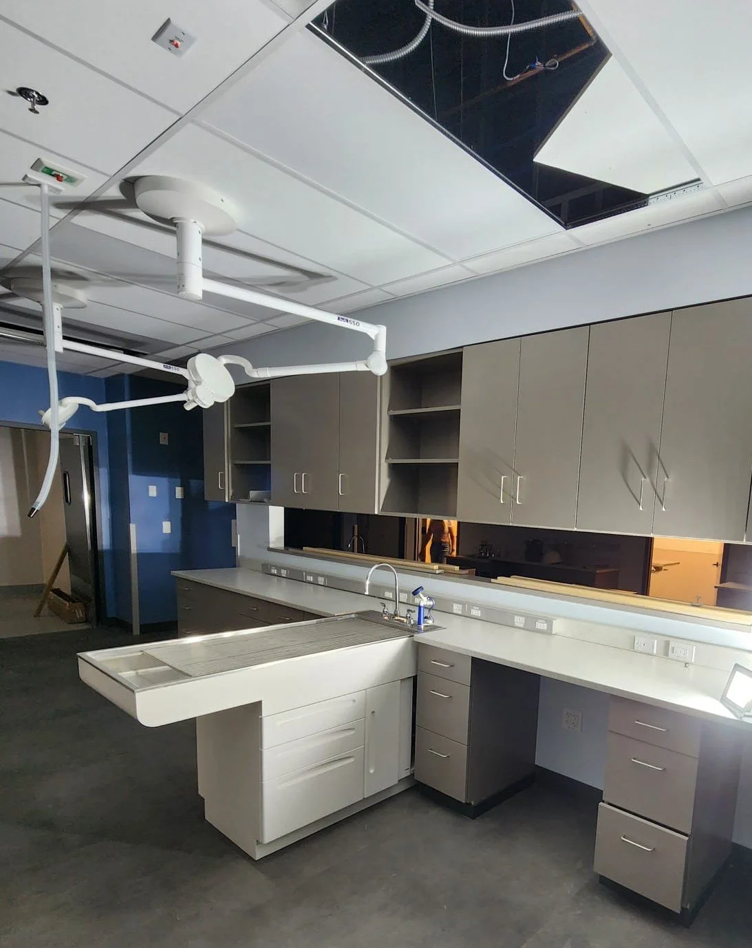 Hospital or laboratory kitchen with overhead surgical lights, cabinetry, and a sink, suggesting ongoing construction or installation.