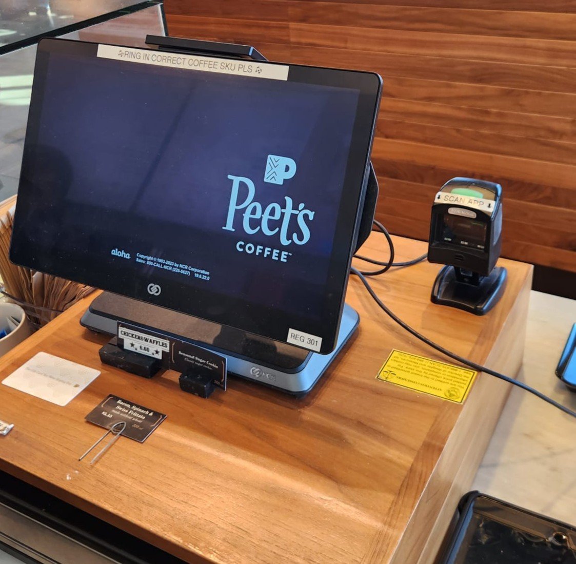 Self-service coffee checkout station at Peet's Coffee with a touchscreen monitor and a card scanner on a wooden counter.
