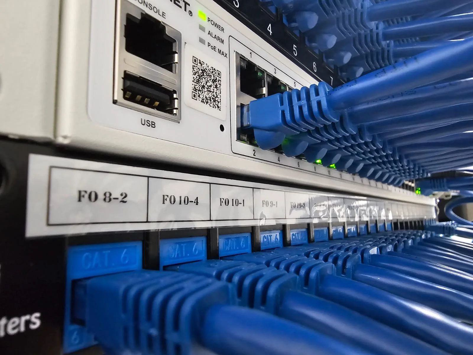 Close-up of a network switch with multiple blue Ethernet cables plugged into it, along with a panel showing port labels and status lights.